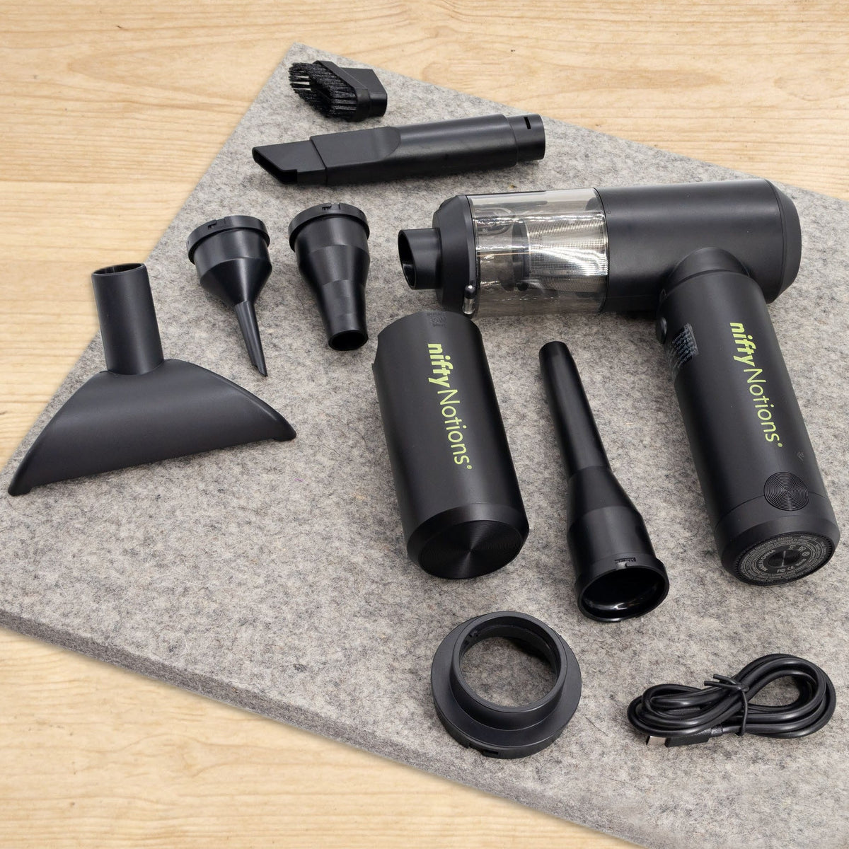 The complete SewClean kit laid out on a gray wool pressing mat: vacuum body, detachable battery, wide flared nozzle, flat crevice nozzle, long precision nozzle, bristle brush, two cone tips, a ring adapter, and the USB-C cable.