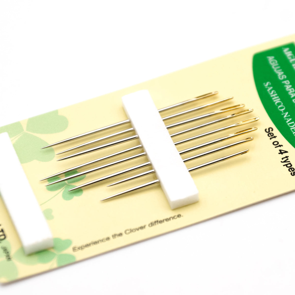 Close view of the Clover sashiko needle card at an angle, showing the gold-plated eyes of the needles held under a white foam strip.