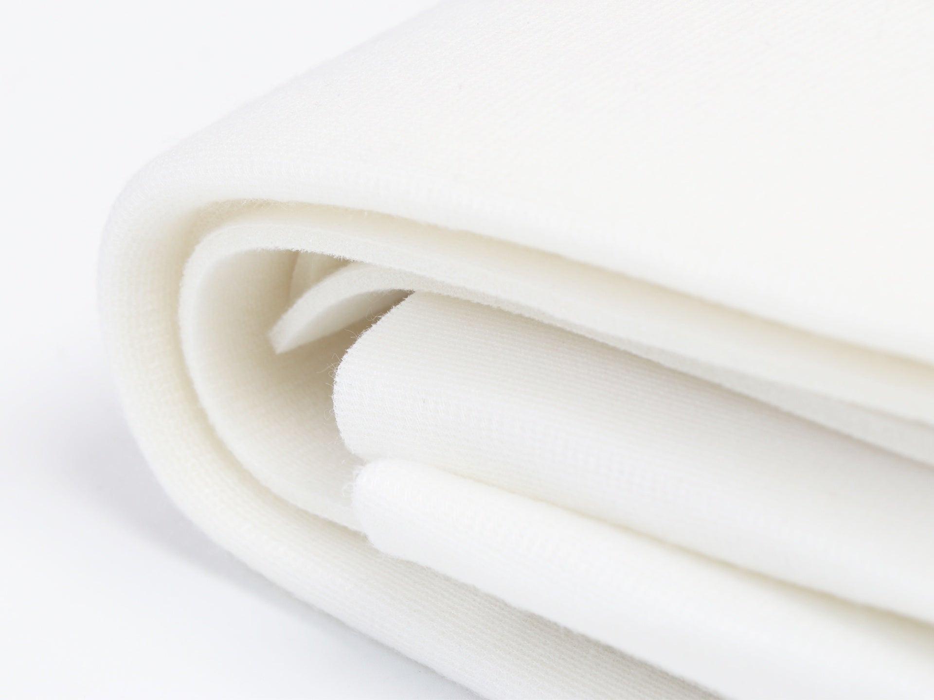 Close-up of ByAnnie's Soft and Stable white foam stabilizer, folded to show its cross-section: a polyester foam core faced with soft white fabric on both sides.