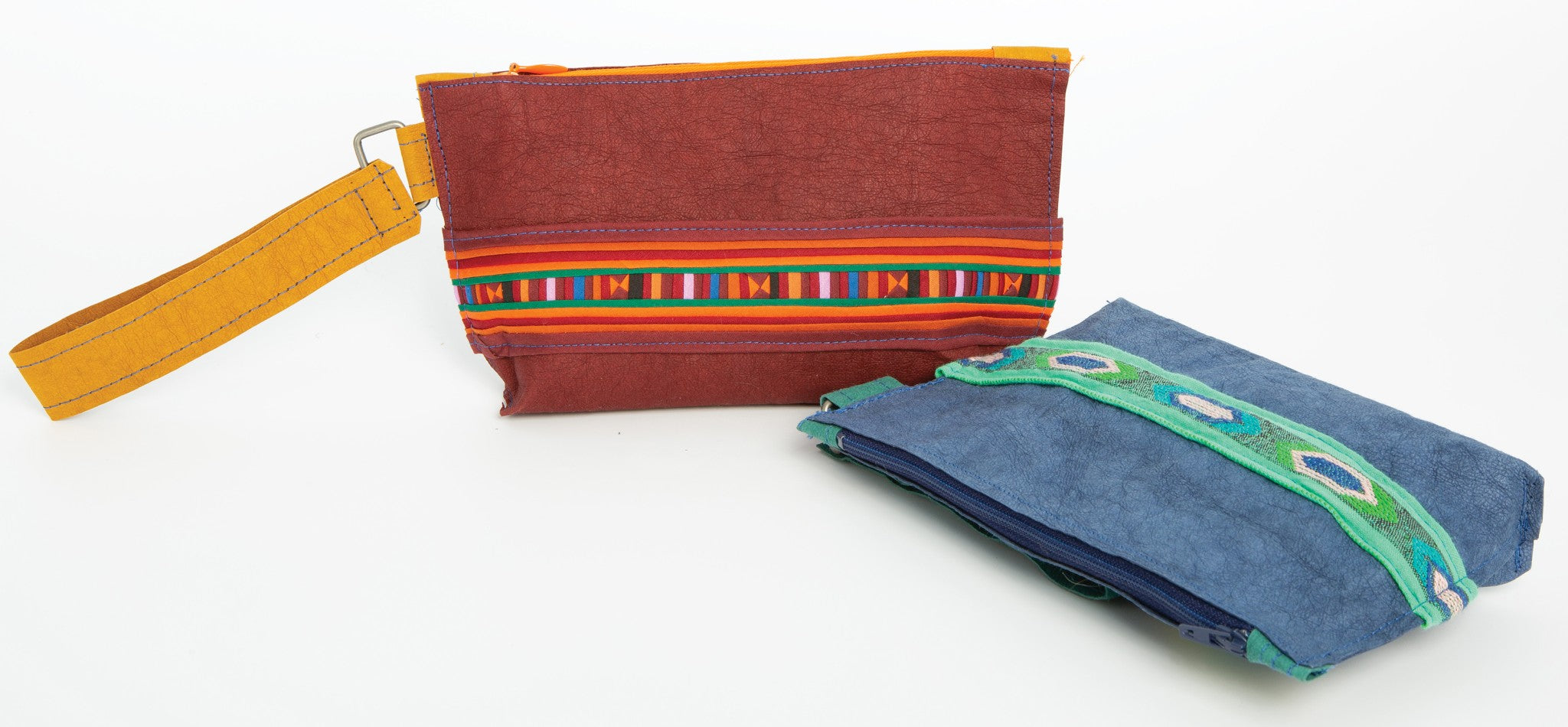 Two zippered pouches made from Kraft-Tex Designer paper fabric, one in Bordeaux with an Ochre wrist strap and woven trim and one in Atlantic Blue with a green zipper and woven trim, by C&T Publishing.