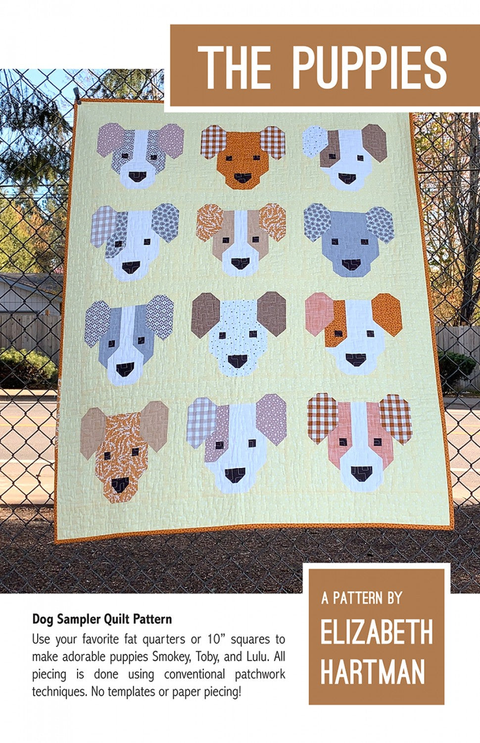 The Puppies quilt pattern cover by Elizabeth Hartman. The 40 by 52 inch small quilt hangs on an outdoor chain-link fence showing 12 patchwork puppy faces in a 3 by 4 grid on a light yellow-green background. Each puppy has two coordinating dog fabrics for ears and face, a white muzzle, and dark eyes and nose in gray, orange, blue, tan, pink, and multicolor colorways.