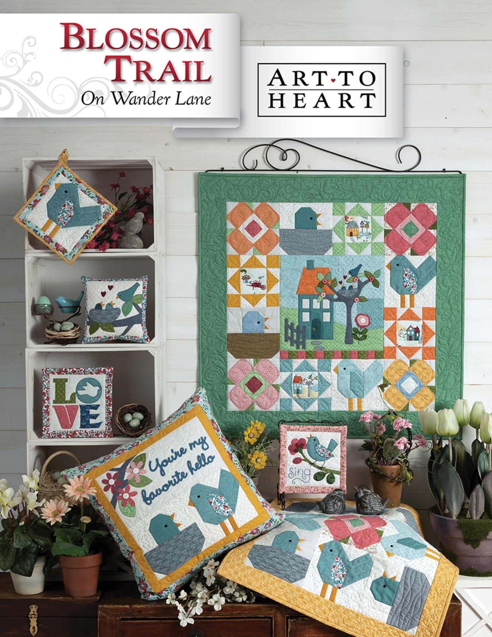 Front cover of the Blossom Trail on Wander Lane quilt pattern by Nancy Halvorsen, Art to Heart, showing the bluebird and spring flower appliqué block framed in patchwork with a favorite hello pillow and bluebird projects.