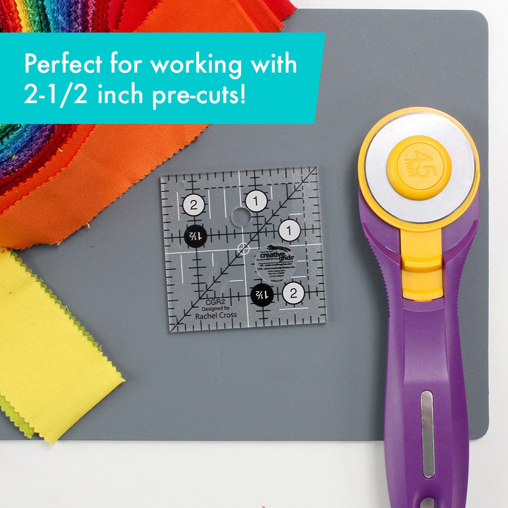 Creative Grids 2-1/2 inch square ruler CGR2 on a gray cutting mat beside a rotary cutter and a stack of 2-1/2 inch precut strips, captioned Perfect for working with 2-1/2 inch pre-cuts.