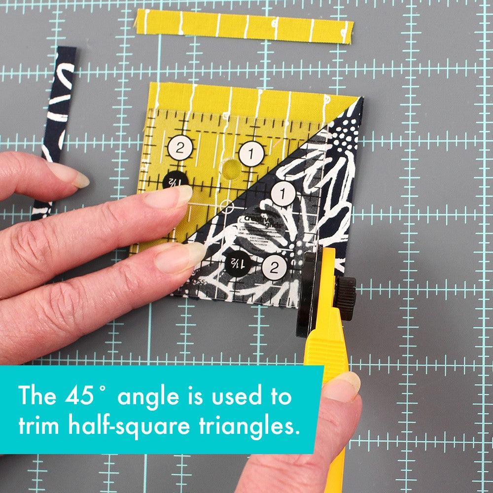 Creative Grids 2-1/2 inch square ruler CGR2 with its 45 degree line on the seam of a yellow and black half-square triangle while a rotary cutter trims it, with a caption about trimming half-square triangles on the 45 degree angle.
