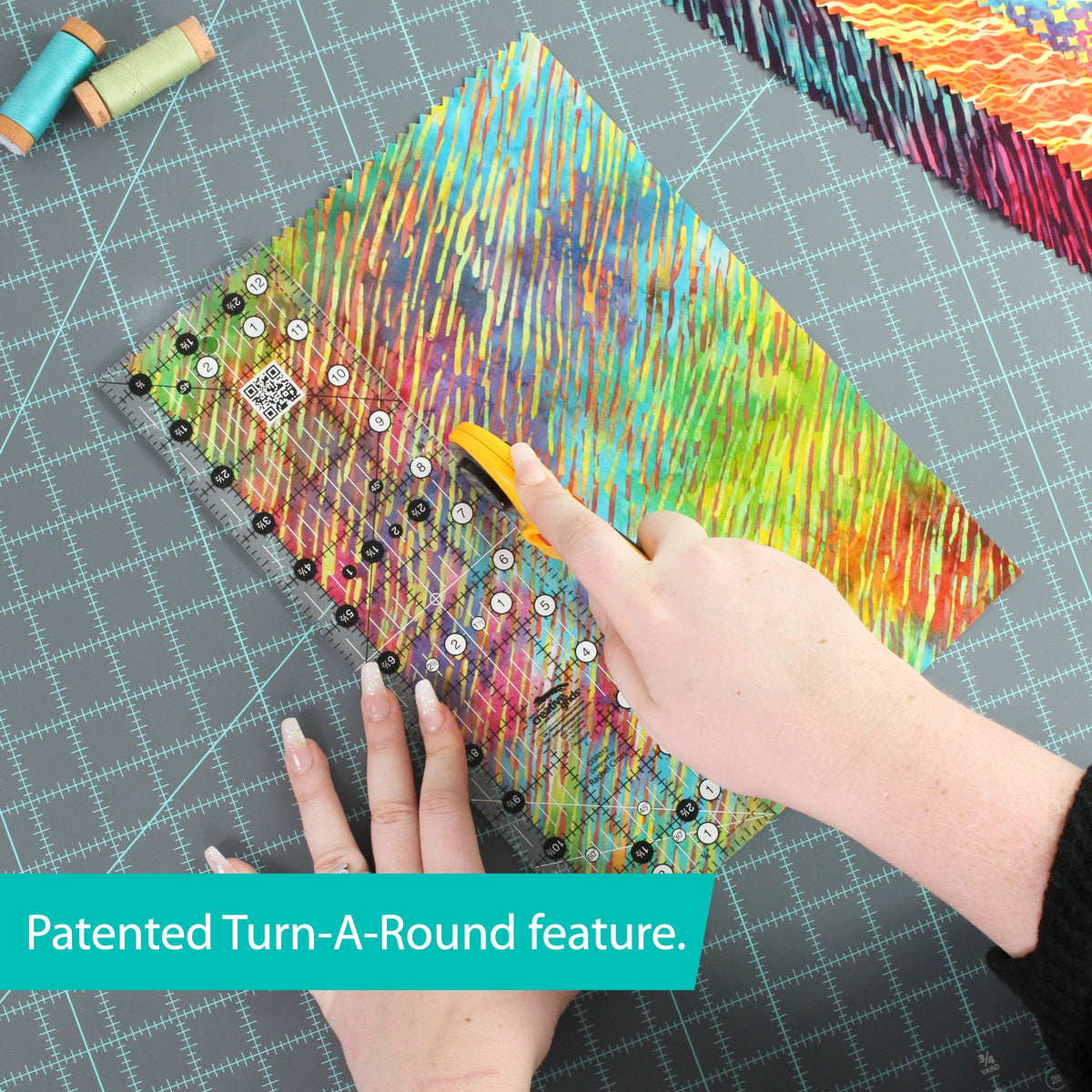 Creative Grids 3-1/2 x 12-1/2 inch ruler CGR312 on multicolor batik fabric with a hand turning it, with a brand caption about the patented Turn-a-Round feature.