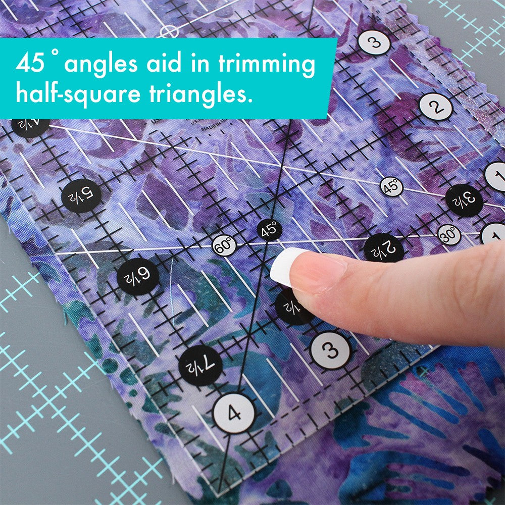 Close-up of the crossed 45 degree lines on the Creative Grids 4-1/2 x 8-1/2 inch ruler CGR48 over purple batik fabric, with a brand caption about trimming half-square triangles.