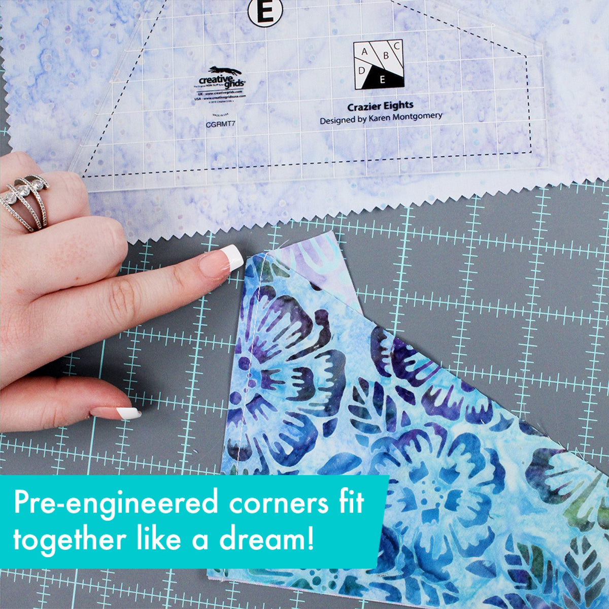 Close view of two blue batik patches sewn together, with a person's finger at the point where the blunt corner of one patch meets the edge of the other. Template E of the Creative Grids Crazier Eights Templates CGRMT7 lies on pale blue fabric above. A caption says the trimmed corners fit together.