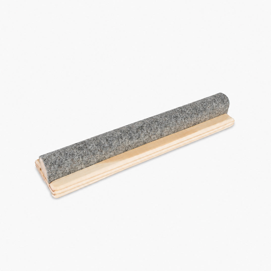 The Gypsy Quilter 12-inch Wool Pressing Bar with clapper at an angle on a light background, a gray wool-covered rounded top mounted along a light wood base with a molded edge.