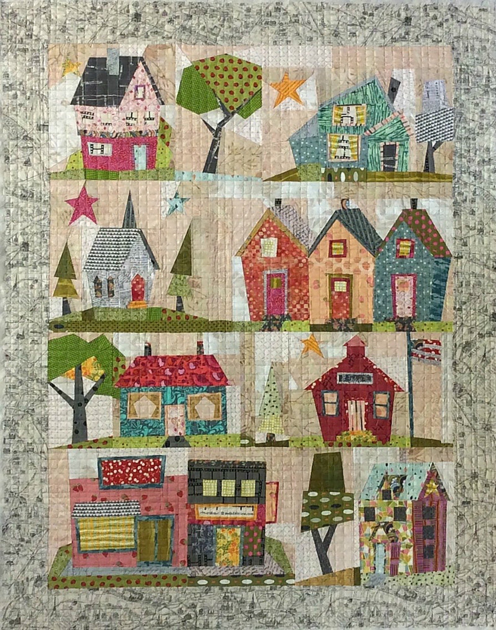 My Kinda Town paper pieced quilt by Peggy Larsen for Fiberworks. Four rows of whimsical tilted buildings including a pink two story house, a white steepled church, a row of three cottages, a red schoolhouse with bell tower, and a corner shop, with polka dot trees and scattered stars between them, framed by a pale map print border. Finished size 42 x 54 inches.