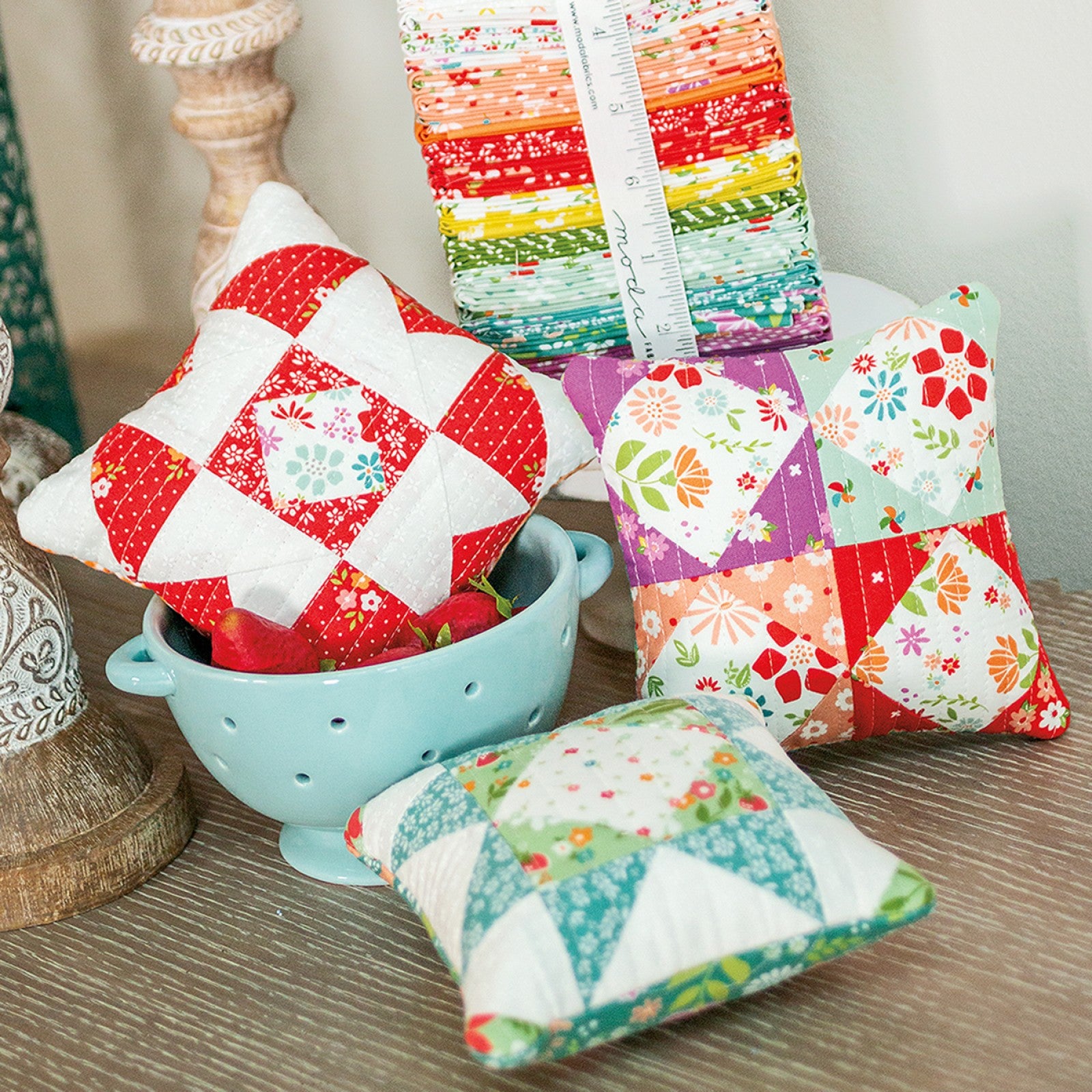 Family Favorites pillows and small pincushions in bright prints arranged around a blue bowl.