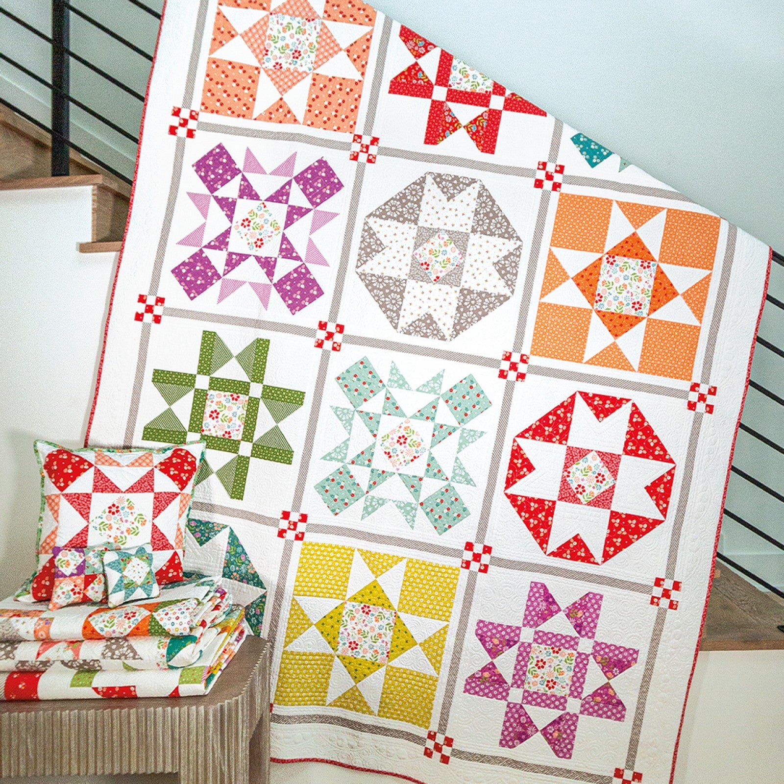 A Family Favorites sampler quilt of pieced star blocks in bright prints on white, hung on a staircase.