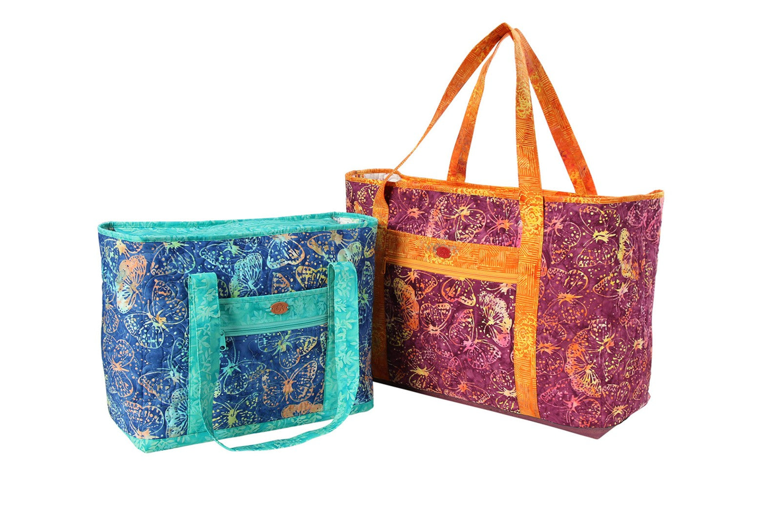 Two finished Two Big Totes in batik butterfly prints, a smaller blue and teal tote beside a larger purple and orange tote, both with quilted bodies and shoulder straps.