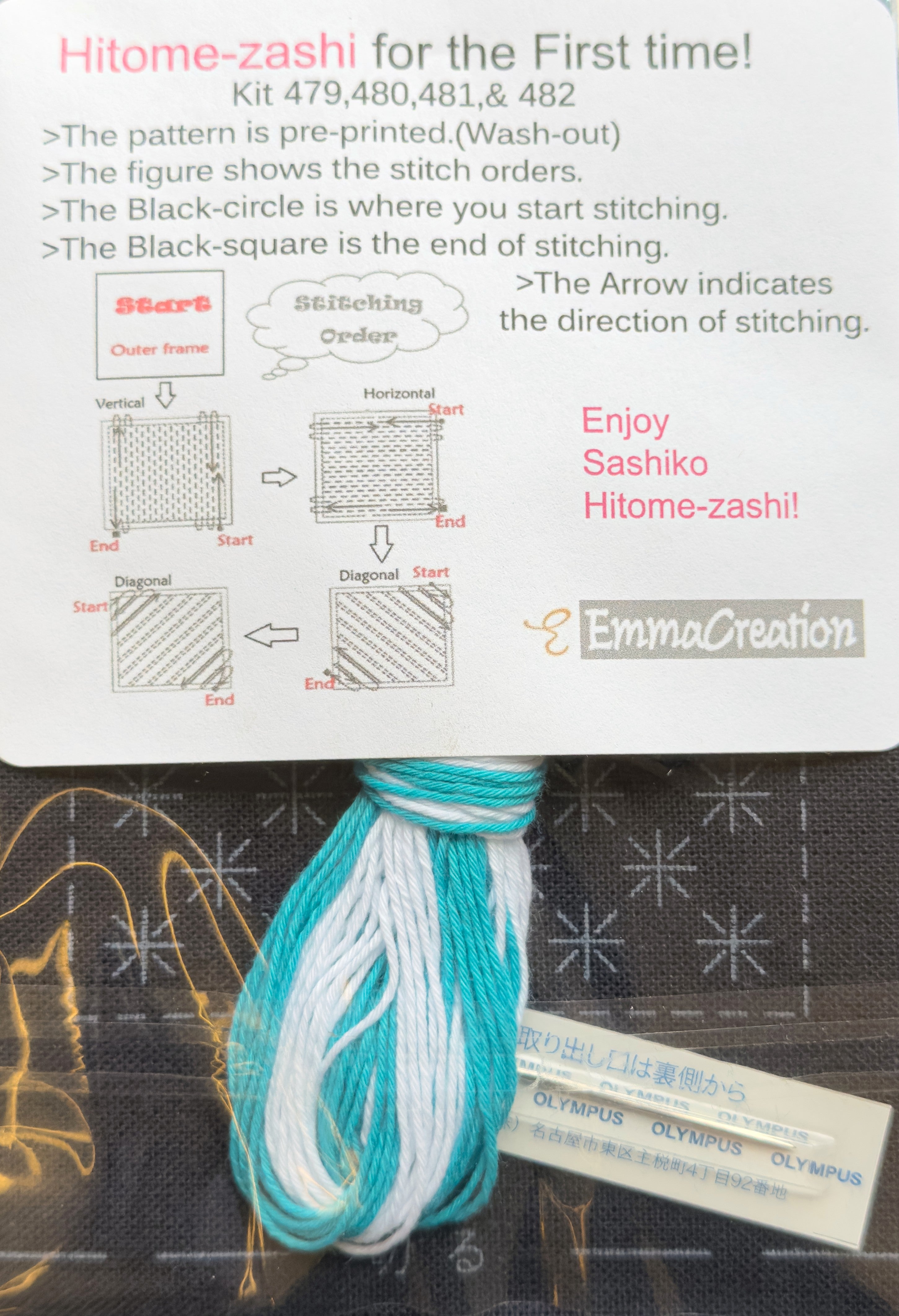 Contents of the Olympus hitomezashi sashiko coaster kit SK-0479 Igeta Navy from EmmaCreation: skeins of aqua and white sashiko thread and an Olympus sashiko needle rest on the navy preprinted cloth, its kome-zashi rice stitch design showing in wash-out ink, beneath the EmmaCreation starter card diagramming the vertical, horizontal, and diagonal stitching order.