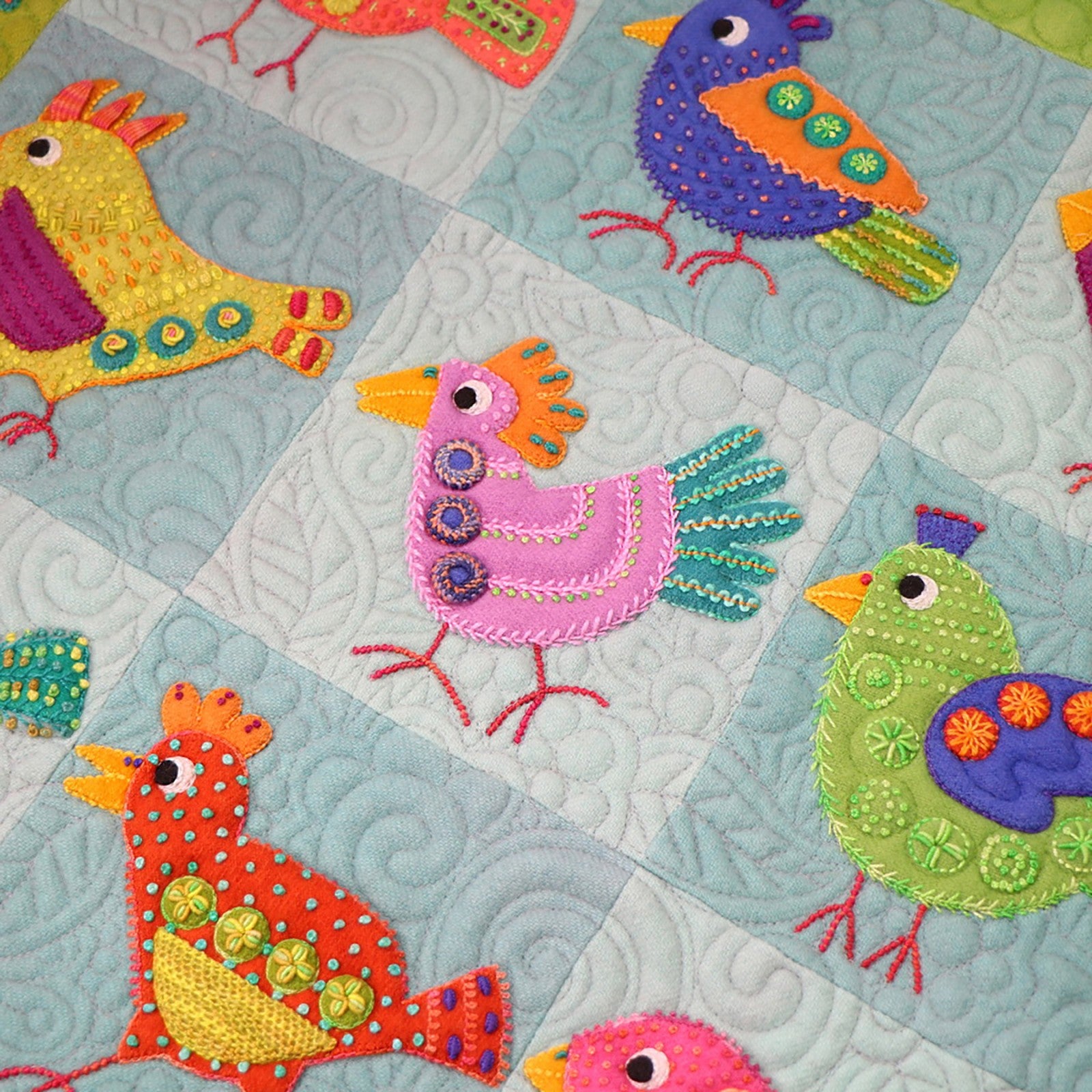 Close detail of several blocks from the Chirp wall hanging by Sue Spargo of Folk Art Quilts. Yellow, purple, pink, green and red wool birds show layered applique with dense hand embroidery on free-motion quilted backgrounds.