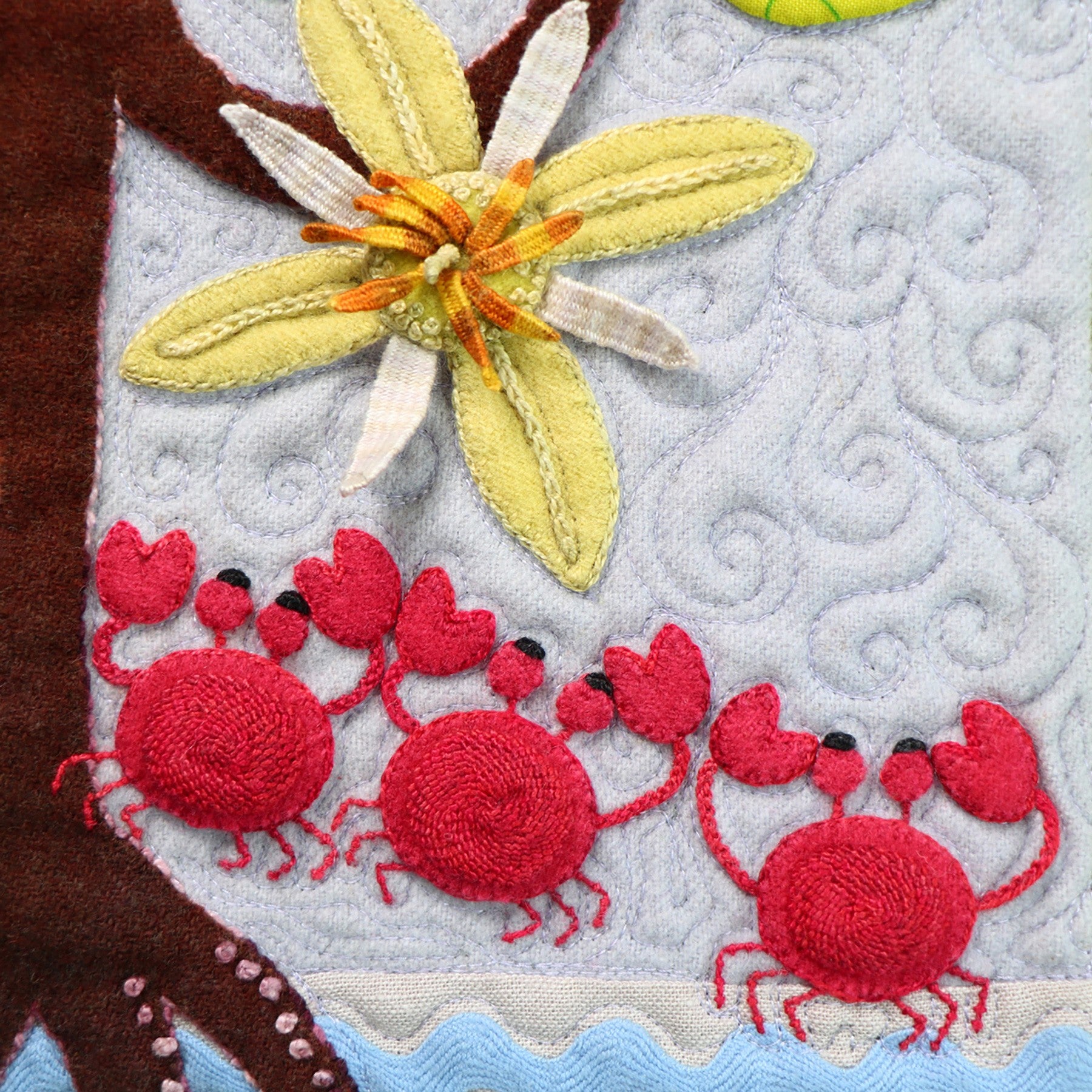 Close-up of a Forest for the Trees block, a yellow flower and red crabs worked in wool applique and textural hand embroidery.