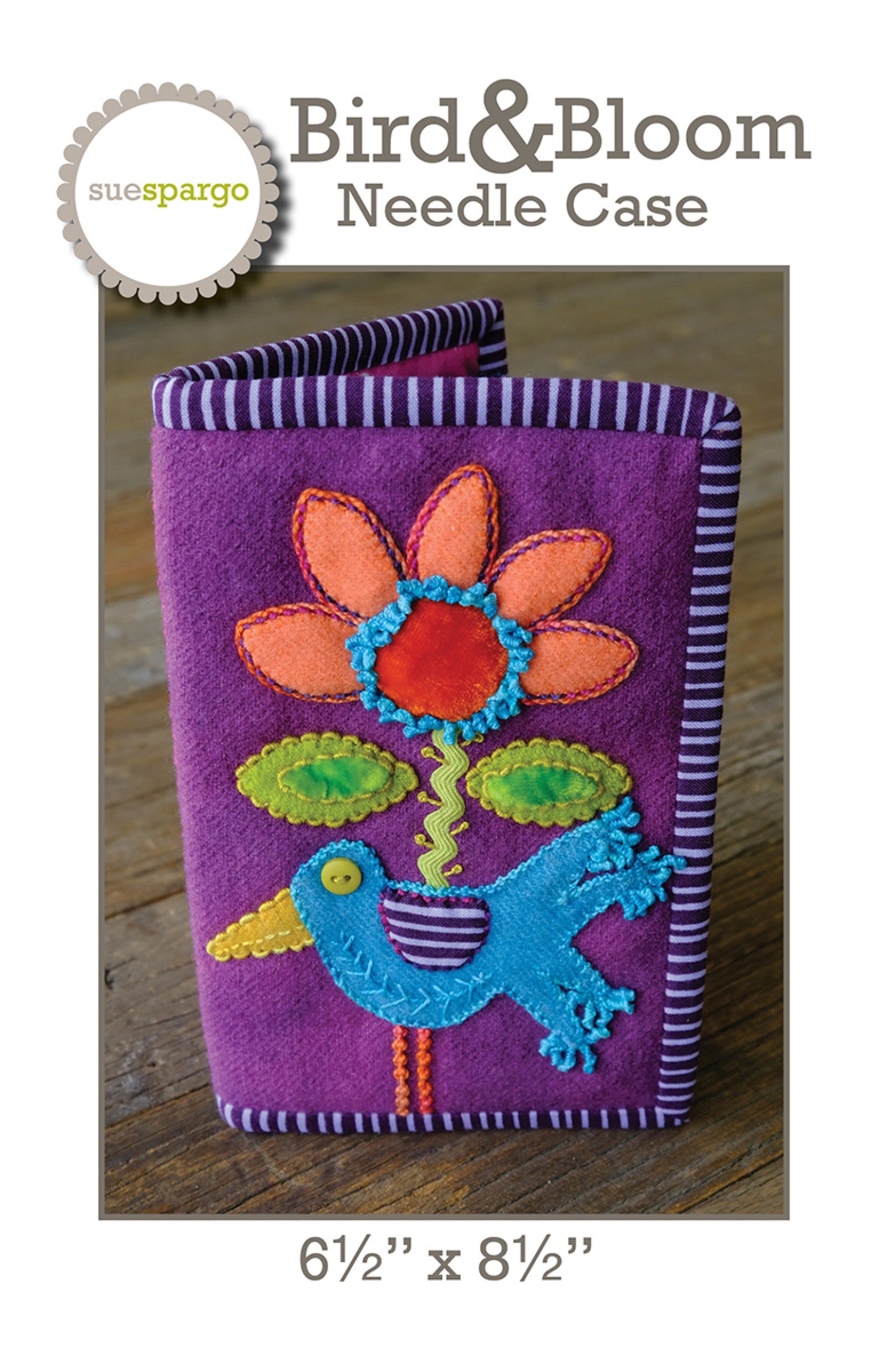 Bird and Bloom Needle Case sewing pattern by Sue Spargo of Folk Art Quilts. Front cover shows the finished needle case in purple wool bound in purple-and-white stripe, with a folk-art appliqué design: a coral-petaled flower with a layered center on a rick-rack stem, green leaves, and a turquoise bird with a striped wing, all richly hand embroidered. Size 6-1/2 by 8-1/2 inches shown.
