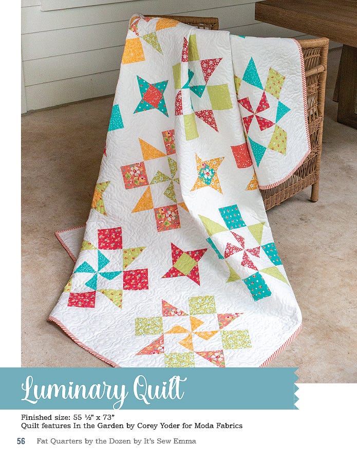 The Luminary quilt, 55.5 x 73 inches, sparkling pieced stars in red, green, and blue prints on white, hung outdoors.