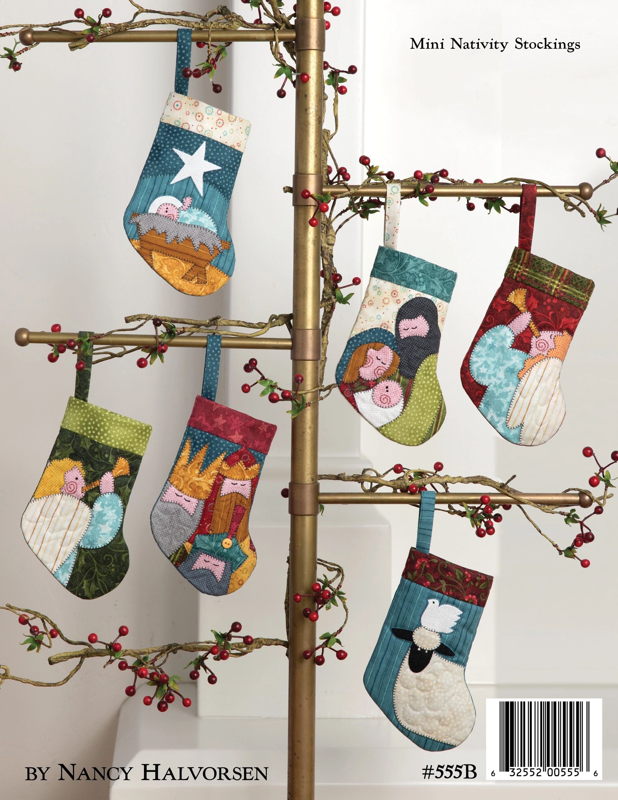 Back cover of the Good Cheer quilt pattern book by Nancy Halvorsen of Art to Heart, showing mini nativity stocking ornaments hung on a branch stand, each appliqued with nativity figures. Marked number 555B by Nancy Halvorsen.