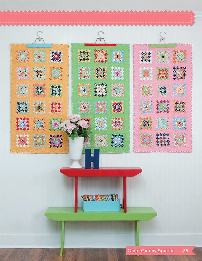 Interior page from the Great Granny Squared quilt pattern book by Lori Holt for It's Sew Emma, showing three small granny-square quilts in gold, green, and pink hung in a row on a white wall above a red bench holding a white vase of pink flowers and a box of fabric strips.