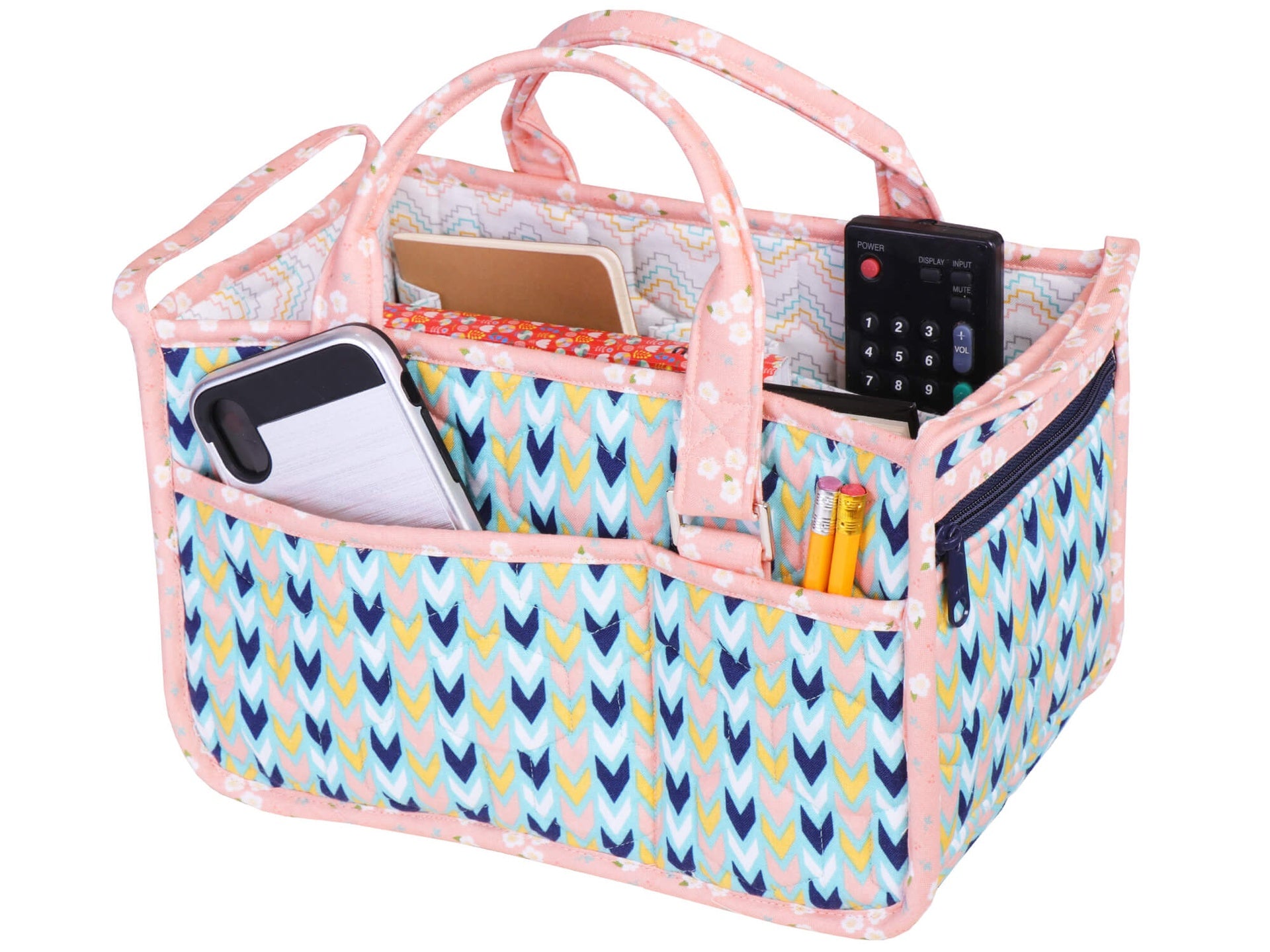 Top-down view inside the In Control Caddy in a teal arrow print with pink binding, showing the expanding dividers separating a phone, a remote, and pencils in the lined compartments.