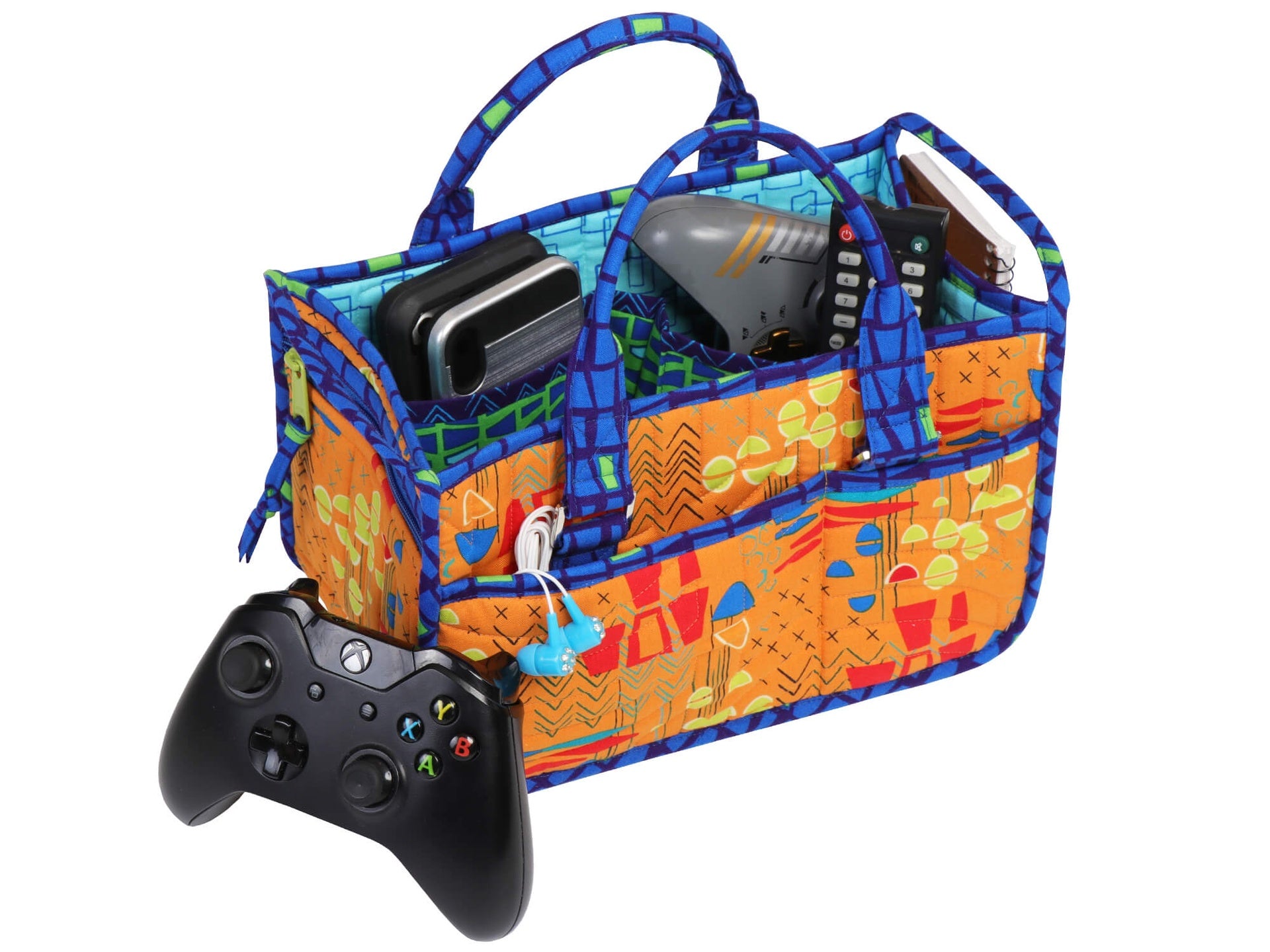 In Control Caddy sewn in a bright orange print, holding a game controller, a tablet, and cables, used as a desk caddy for electronics.