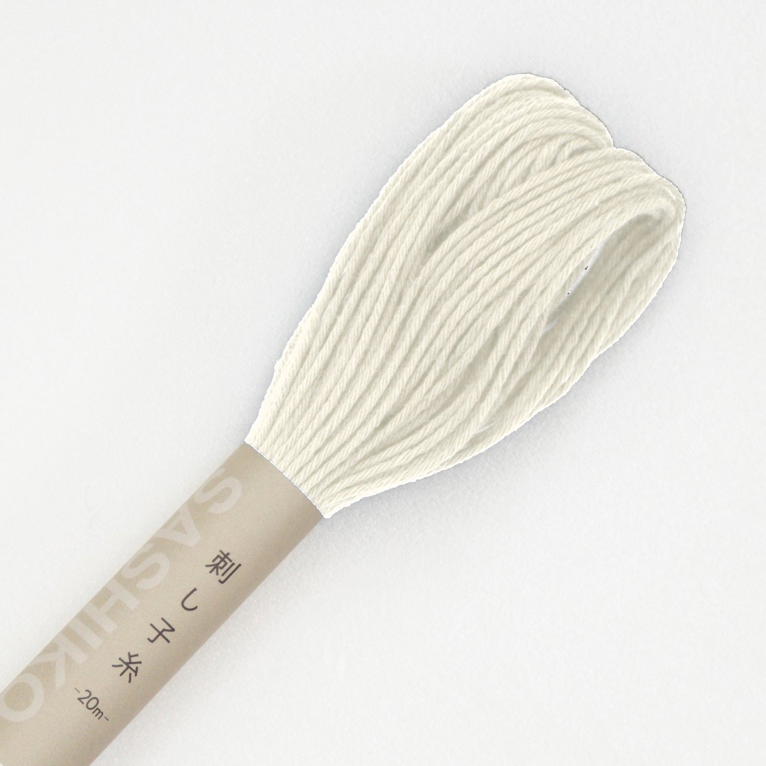 Olympus sashiko thread in off white, a close view of the looped end of an unbleached ecru cotton skein above its kraft SASHIKO paper band, on a white background.