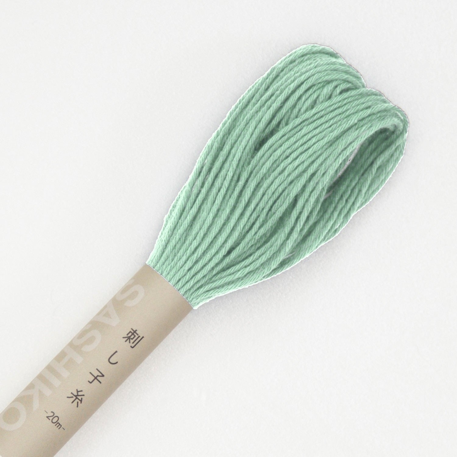 Olympus sashiko thread in green, a close view of the looped end of a soft sage-green cotton skein above its kraft SASHIKO paper band, on a white background.