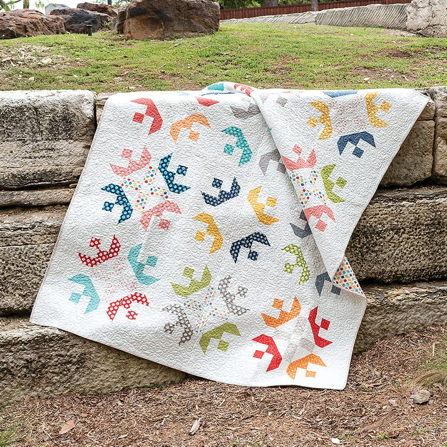 Brioche Quilt from Simply Jelly Rolls, soft scrappy blocks on a white background draped outdoors.
