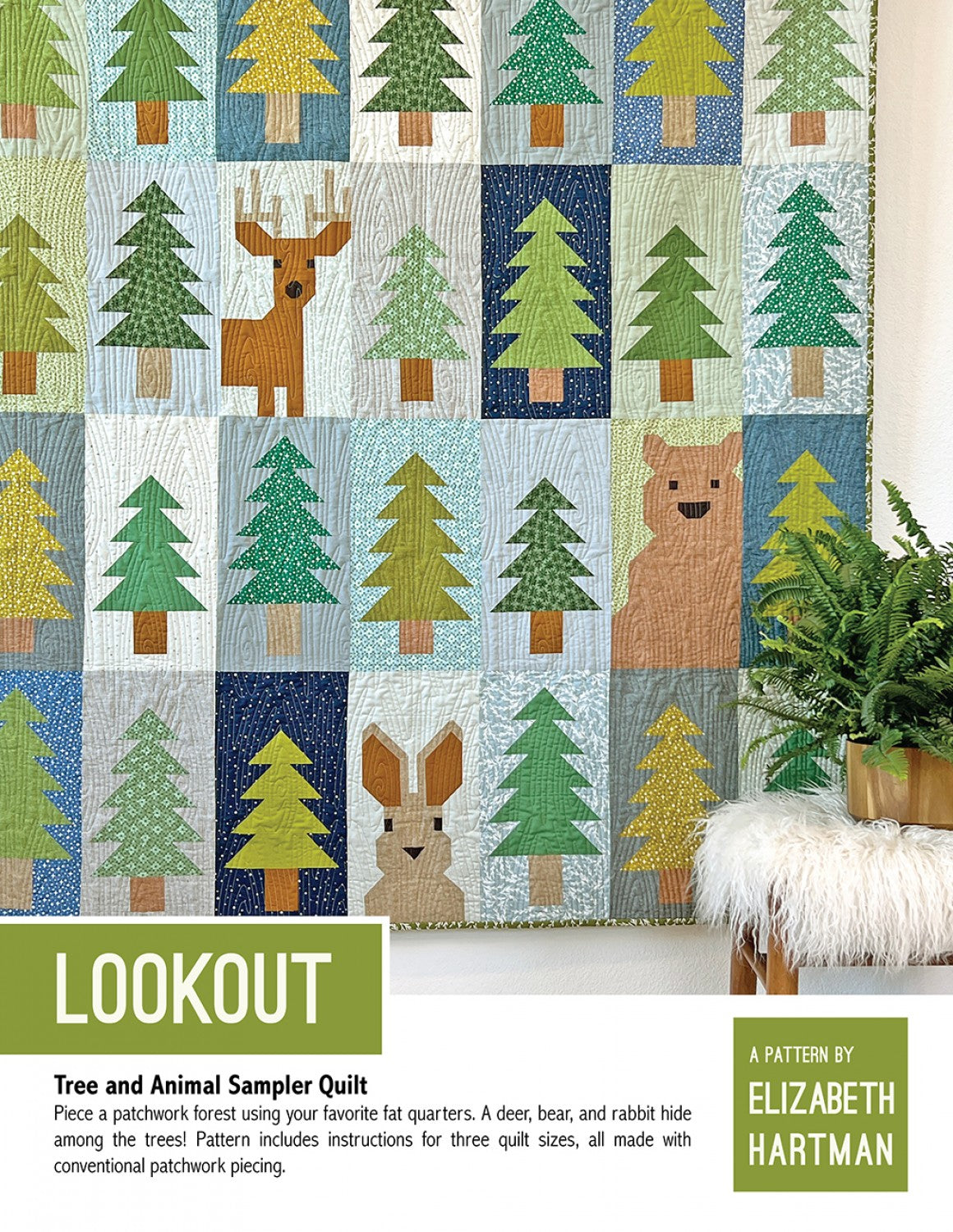 Lookout quilt pattern cover by Elizabeth Hartman. Large 72 by 75 inch picnic quilt hanging on a wall shows patchwork pine trees in shades of green on varied blue, teal, navy, and gray block backgrounds, with a deer showing antlers, a brown bear, and a rabbit with tall ears hiding among the trees. Yellow-green binding visible.