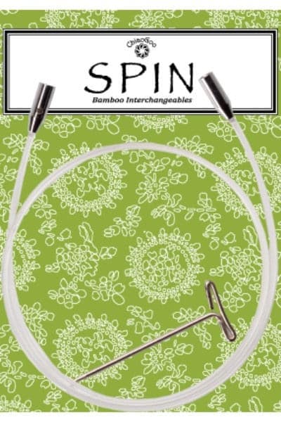 ChiaoGoo SPIN clear nylon interchangeable knitting needle cable shown on its package card. The clear cable lies in a loop over a green card printed with white flowers, with a metal join at each end and a T-shaped tightening key inside the loop. The header reads ChiaoGoo SPIN Bamboo Interchangeables.