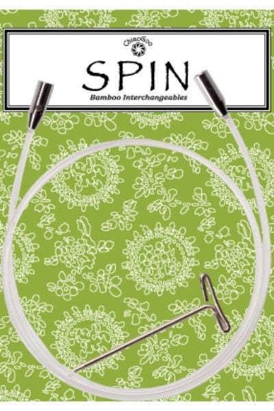 ChiaoGoo SPIN clear nylon interchangeable knitting needle cable shown on its package card. The clear cable lies in a loop over a green card printed with white flowers, with a metal join at each end and a T-shaped tightening key inside the loop. The header reads ChiaoGoo SPIN Bamboo Interchangeables.