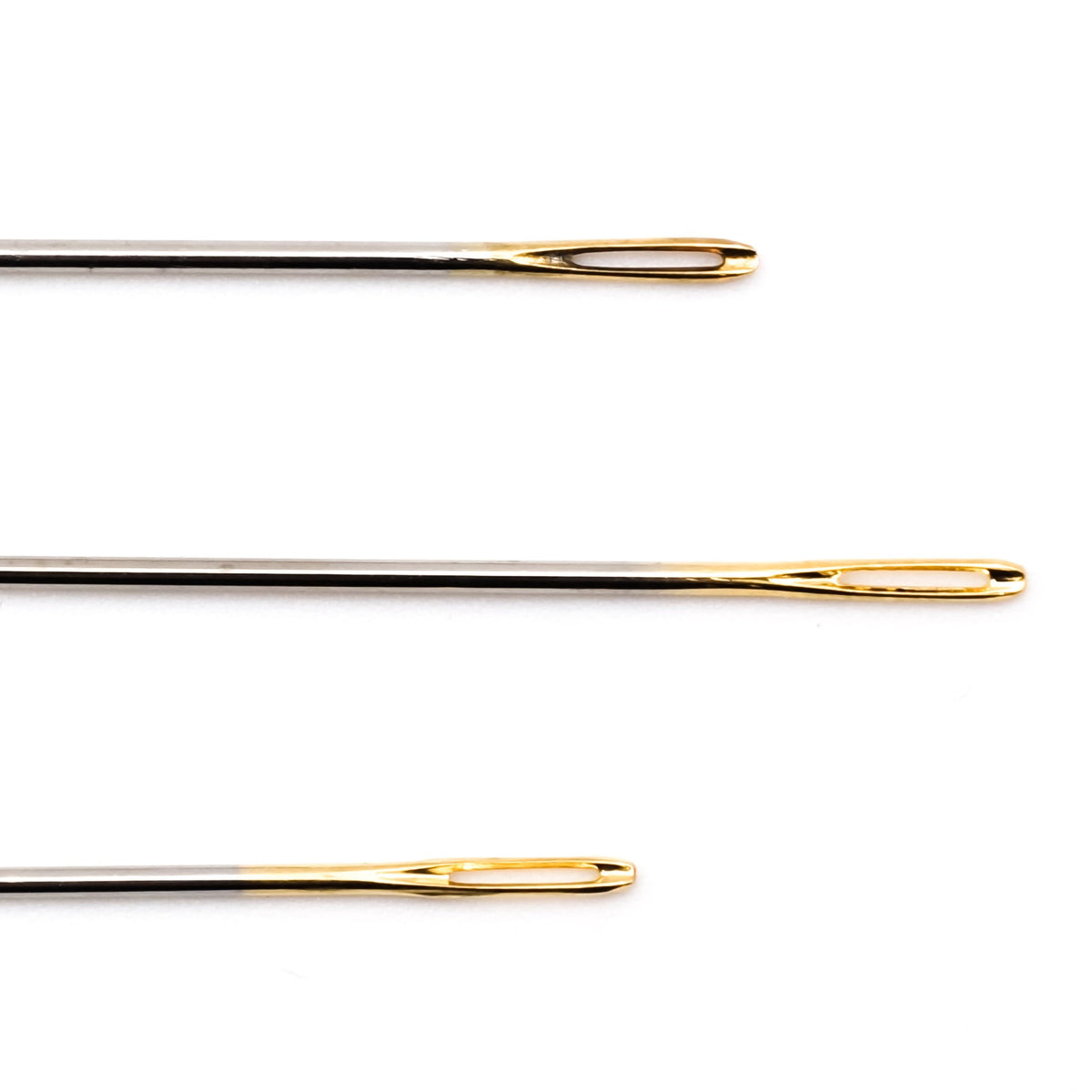 Close view of the gold-plated, elongated eyes of three long Clover sashiko needles.