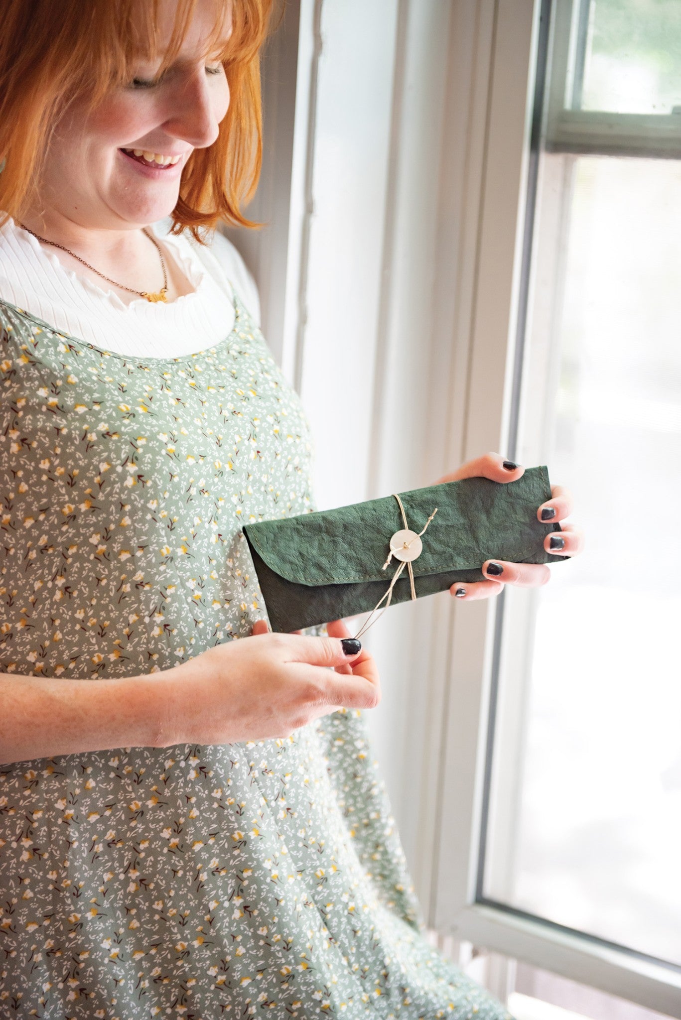 A person holding a folded clutch wallet made from Alpine Green Kraft-Tex Designer paper fabric with a button-and-string closure, by C&T Publishing.