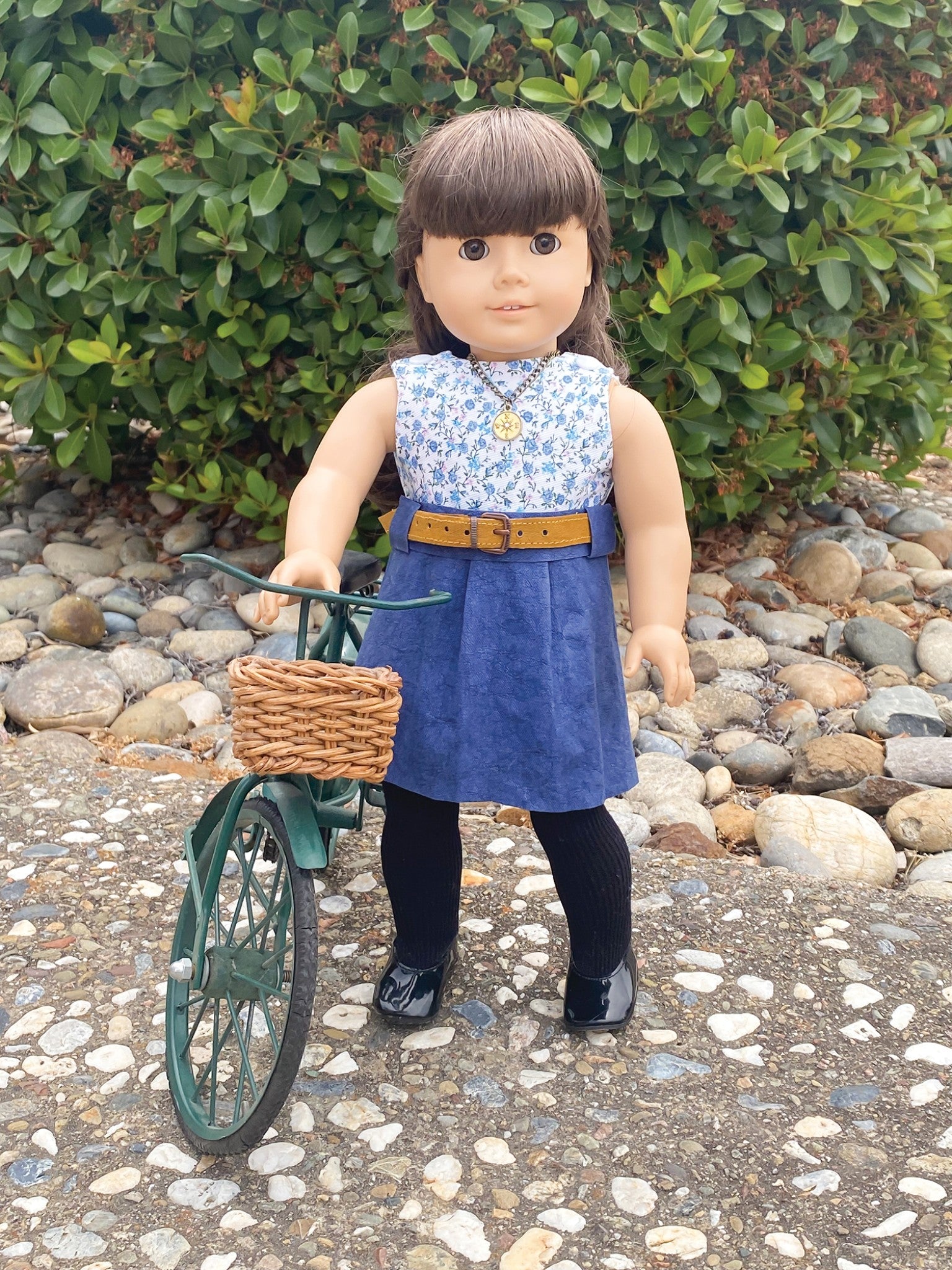 A doll in a handmade dress with an Atlantic Blue Kraft-Tex Designer paper fabric skirt and an Ochre belt, posed with a toy bicycle.
