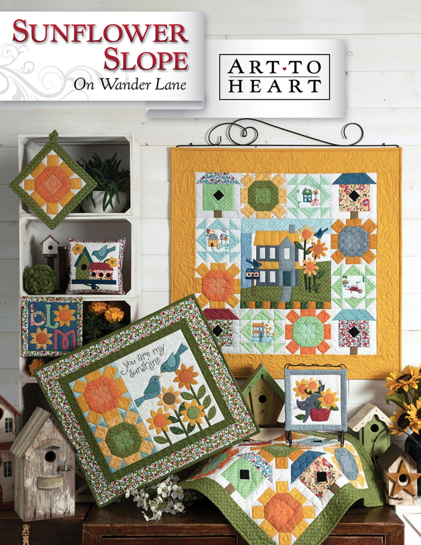 Front cover of the Sunflower Slope on Wander Lane quilt pattern by Nancy Halvorsen, Art to Heart, showing the sunflower and birdhouse appliqué block framed in patchwork with a You Are My Sunshine pillow in golden tones.