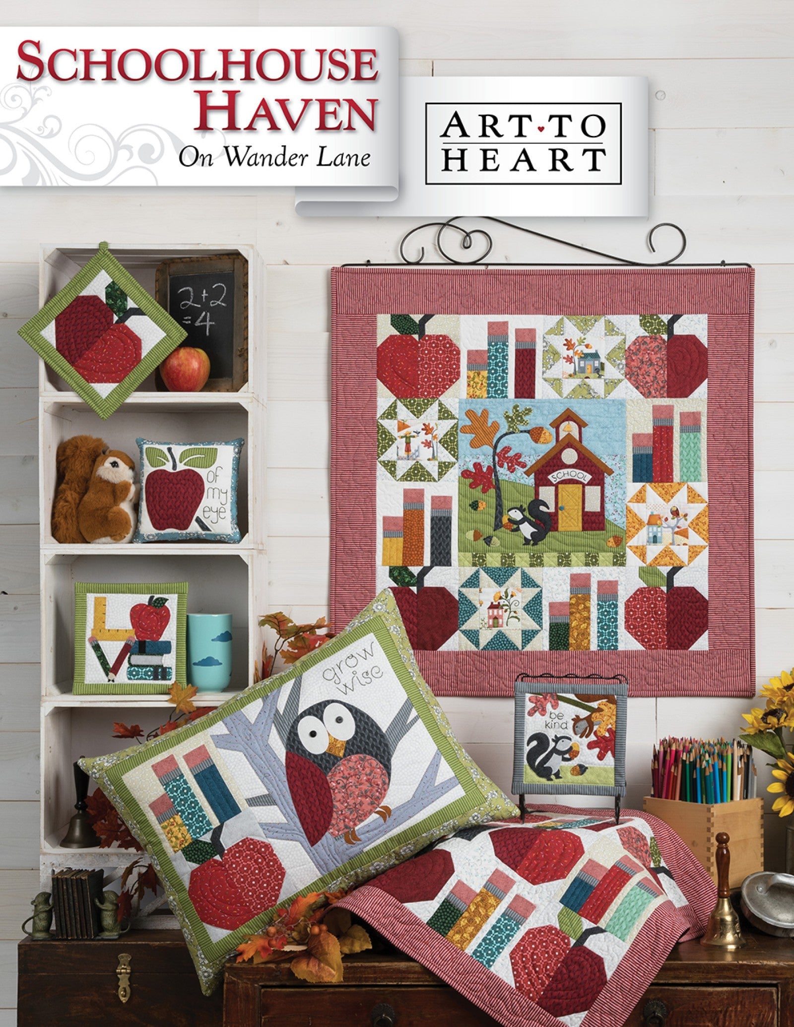 Front cover of the Schoolhouse Haven on Wander Lane quilt pattern by Nancy Halvorsen, Art to Heart, showing the apple and schoolhouse appliqué block framed in patchwork with an owl pillow and back-to-school projects.