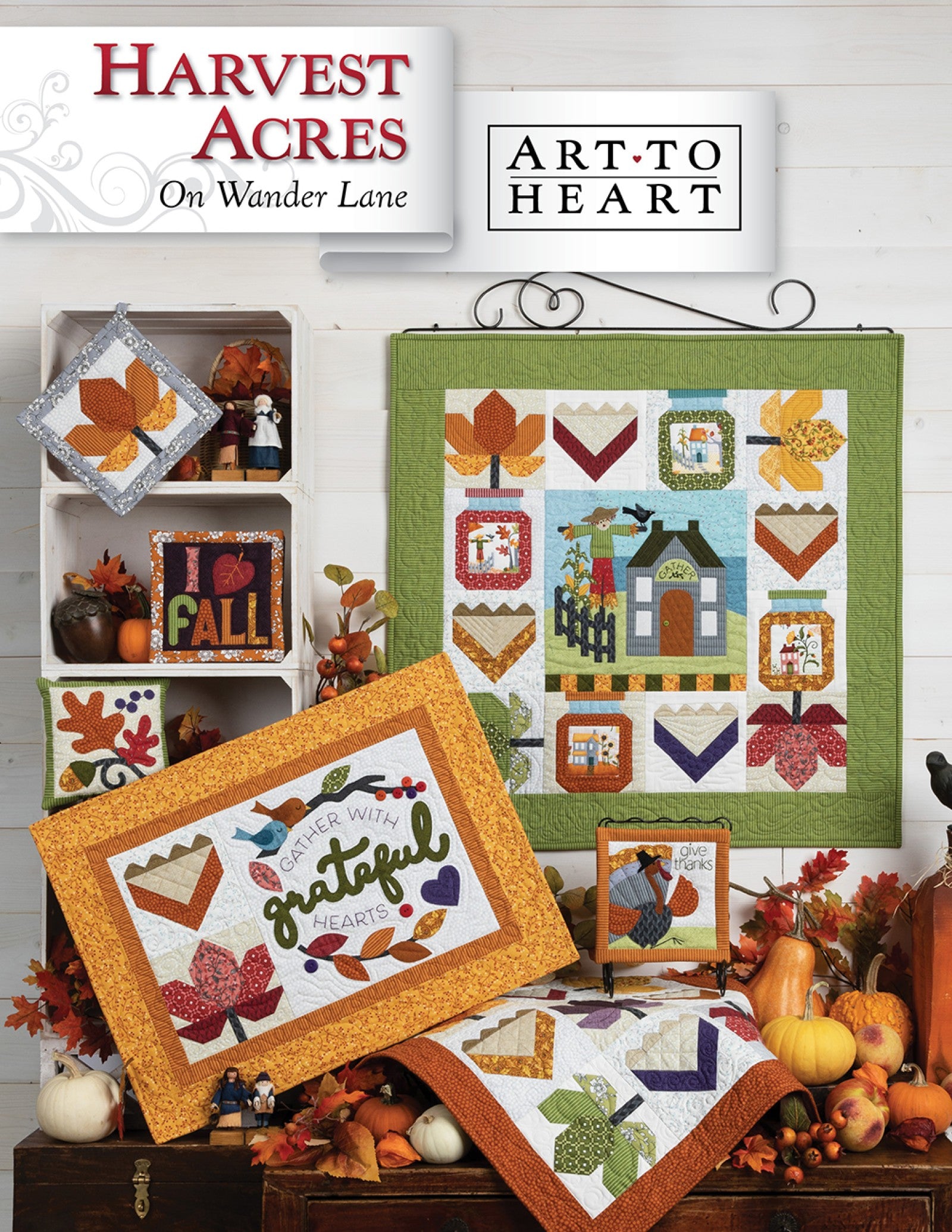 Front cover of the Harvest Acres on Wander Lane quilt pattern by Nancy Halvorsen, Art to Heart, showing the autumn harvest village appliqué block framed in patchwork with a Grateful Hearts quilt and fall leaf projects.