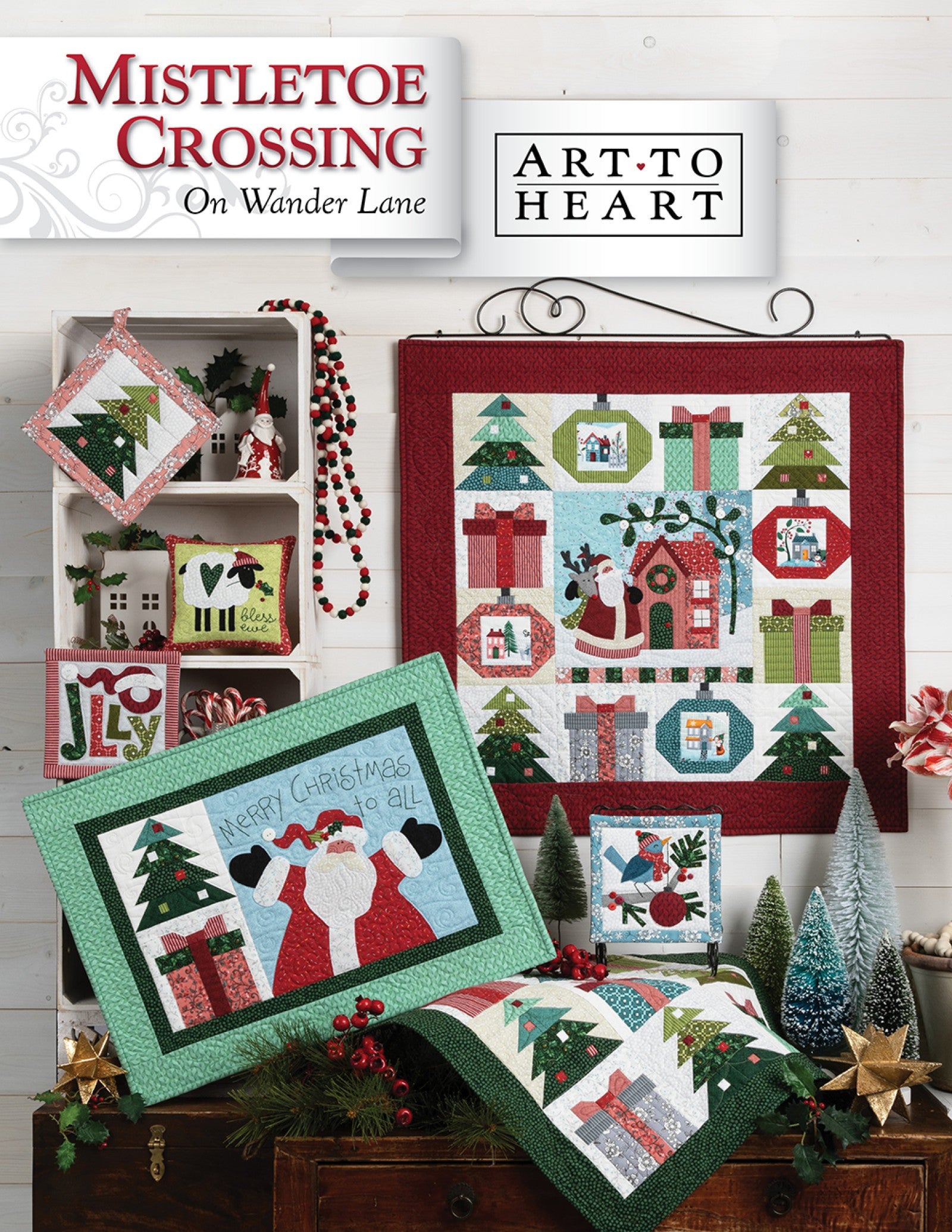Front cover of the Mistletoe Crossing on Wander Lane quilt pattern by Nancy Halvorsen, Art to Heart, showing the Christmas village appliqué block with trees and gifts framed in patchwork with festive holiday projects.