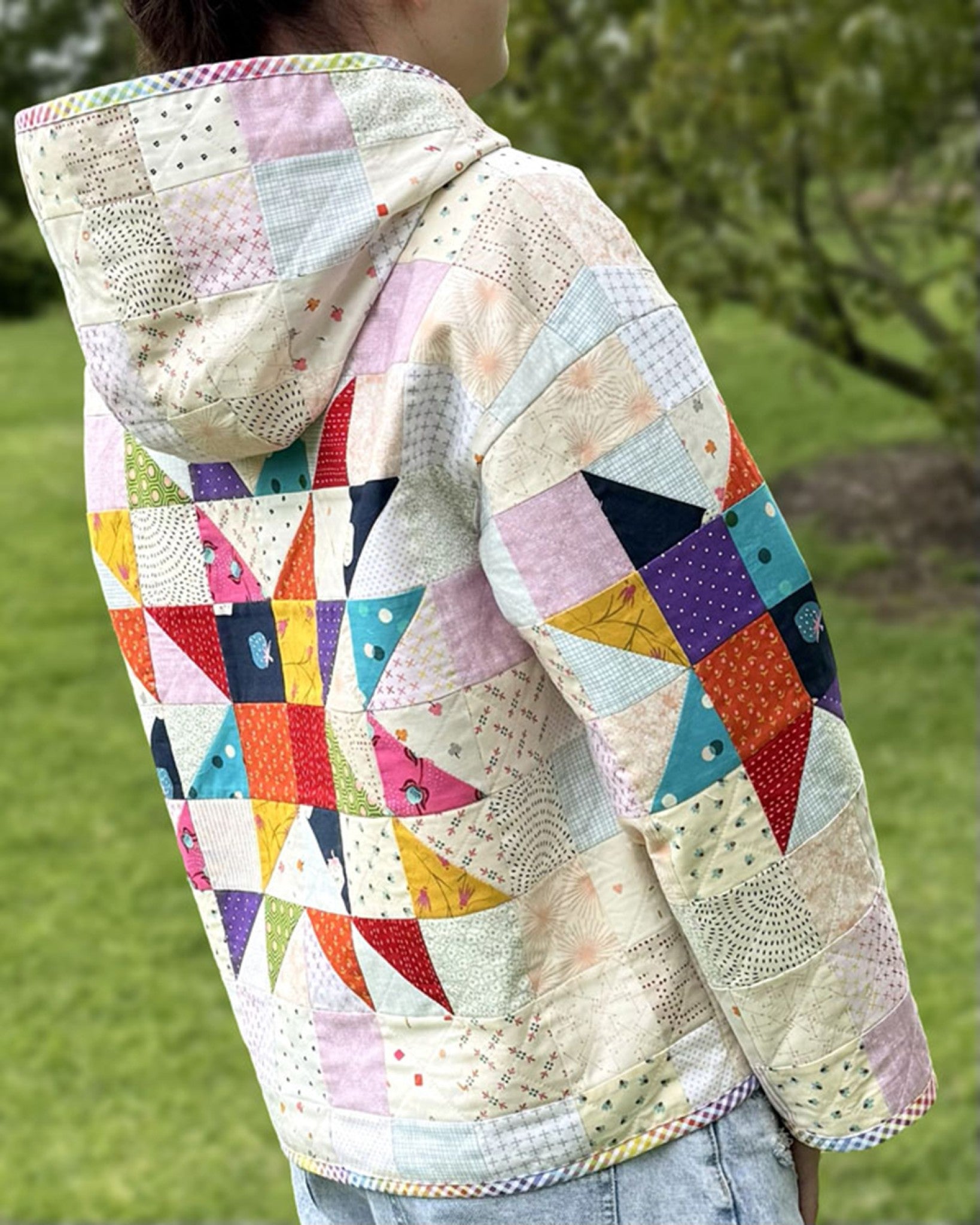 Lexi Hoodie by Melanie McNeice for Melly & Me, back view. The patchwork hoodie seen from behind with the hood down, showing a large pieced star centered on the back and another star on the sleeve, in bright prints on a low-volume background.
