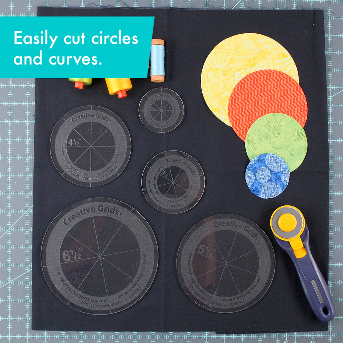 Creative Grids Circles Set of 5 CGRCRCL by Rachel Cross: five clear acrylic circle templates, 2 1/2, 3 1/2, 4 1/2, 5 1/2, and 6 1/2 inches, on black fabric on a gray cutting mat. Each circle has a frosted grip ring with the Creative Grids name, its size, and lines that divide it into eight sections. Four fabric circles in yellow, orange, green, and blue, spools of thread, and a rotary cutter lie beside them. A caption says the templates cut circles and curves.