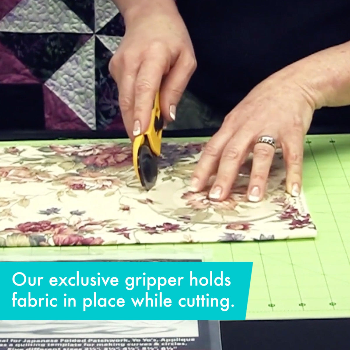 A person holds a clear Creative Grids circle template from the Circles Set of 5 CGRCRCL on floral fabric with one hand and runs a rotary cutter around its edge with the other, on a green cutting mat with a pieced quilt behind. A caption says the gripper holds the fabric in place during cutting.