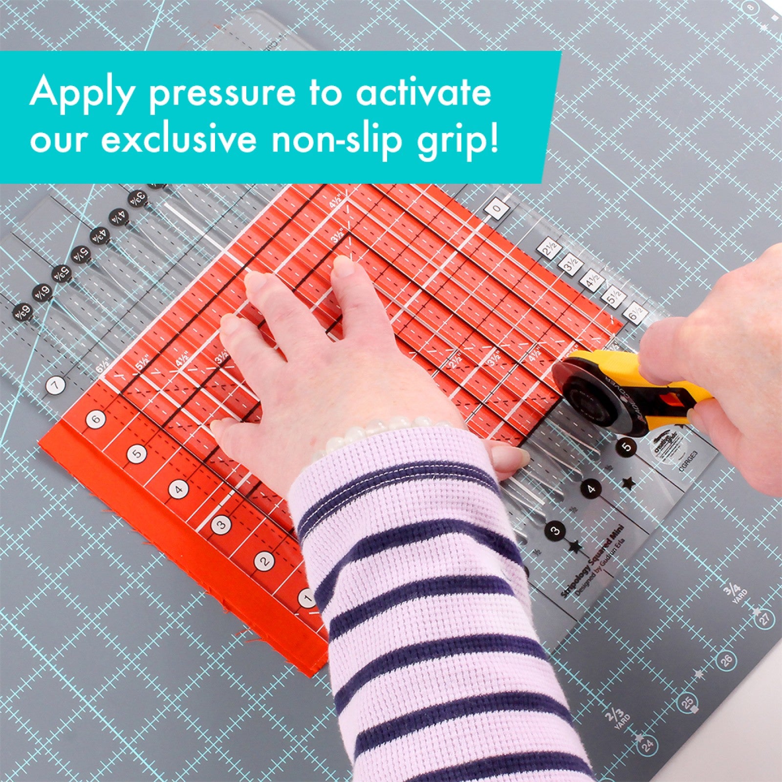 Stripology Squared Mini ruler on a folded stack of fabric with a hand pressing it flat while cutting with a rotary cutter, demonstrating the ruler's non-slip grip activated under pressure.