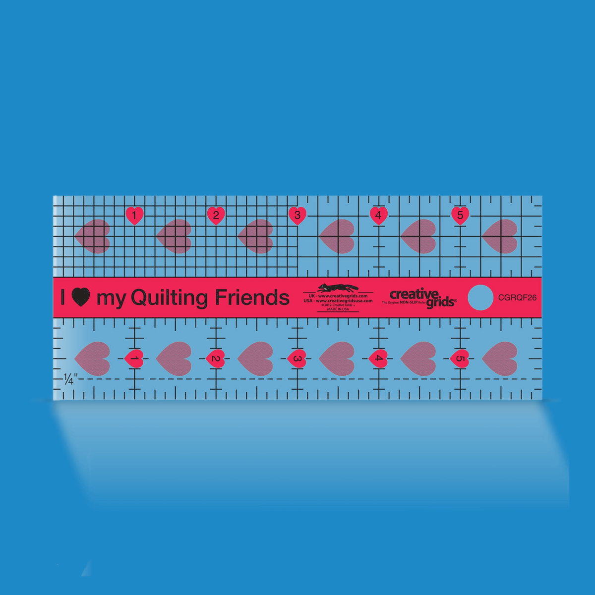 Creative Grids I Love My Quilt Friends Mini ruler CGRQF26 by Rachel Cross on a blue background: pink center band printed I heart my Quilting Friends, 1/8 inch and 1/4 inch grids on the top row, vertical inch lines with a dashed 1/4 inch line on the bottom row, and inch numbers 1 to 5 in pink hearts.