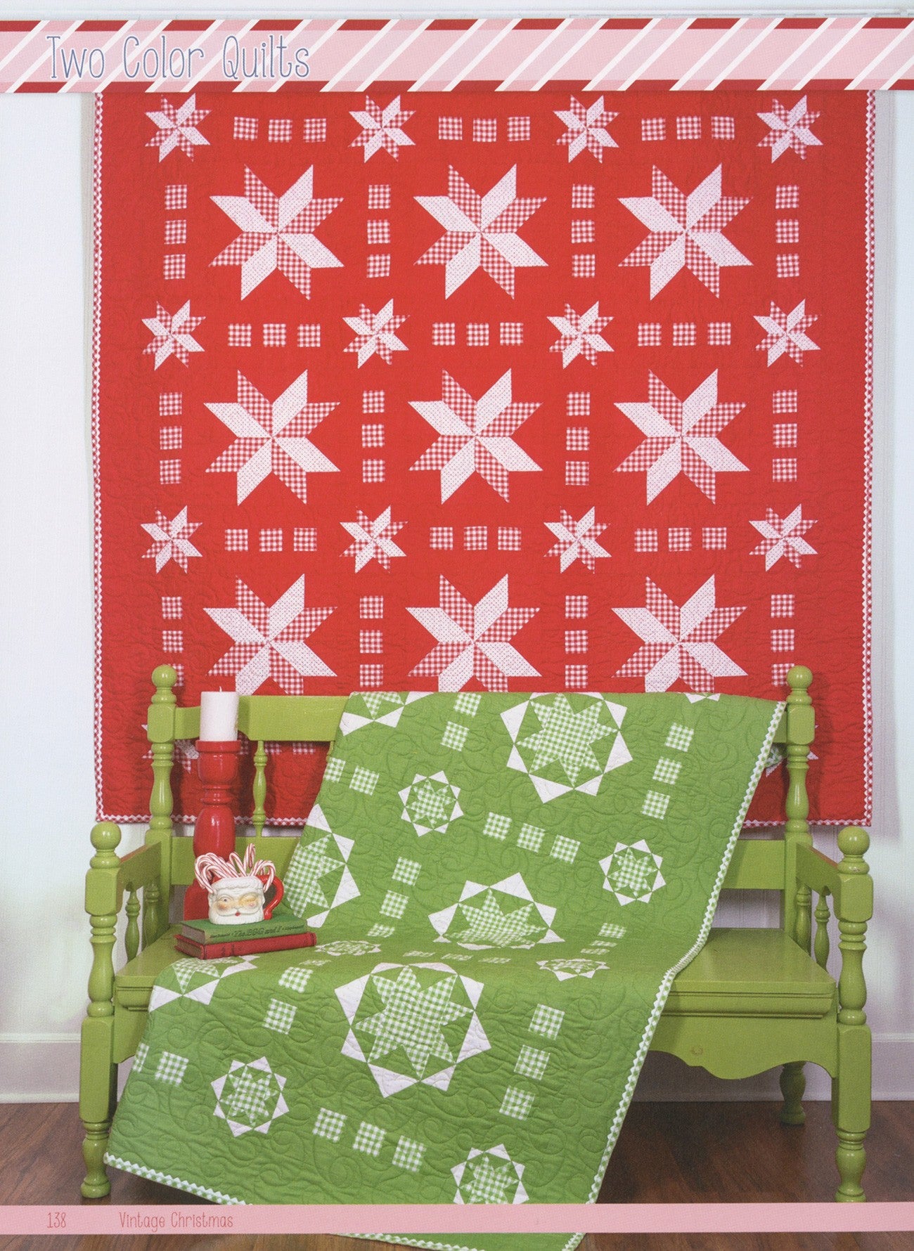 Two Color Quilts from Vintage Christmas by Lori Holt for It's Sew Emma: a red and white star quilt on the wall and a green and white star quilt draped over a green bench with a red candle and a Santa mug.