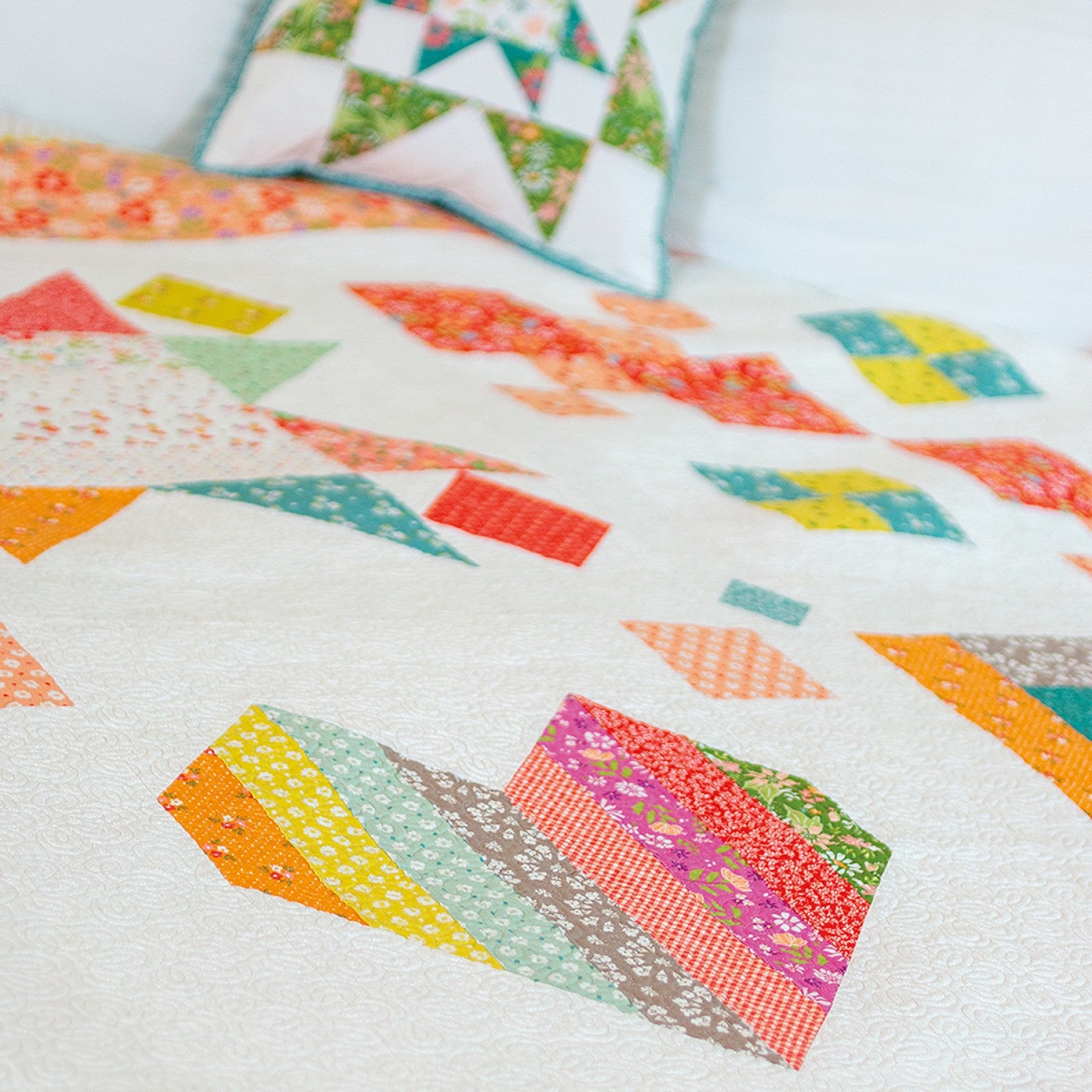 A scrappy Family Favorites sampler quilt in bright prints draped over furniture.