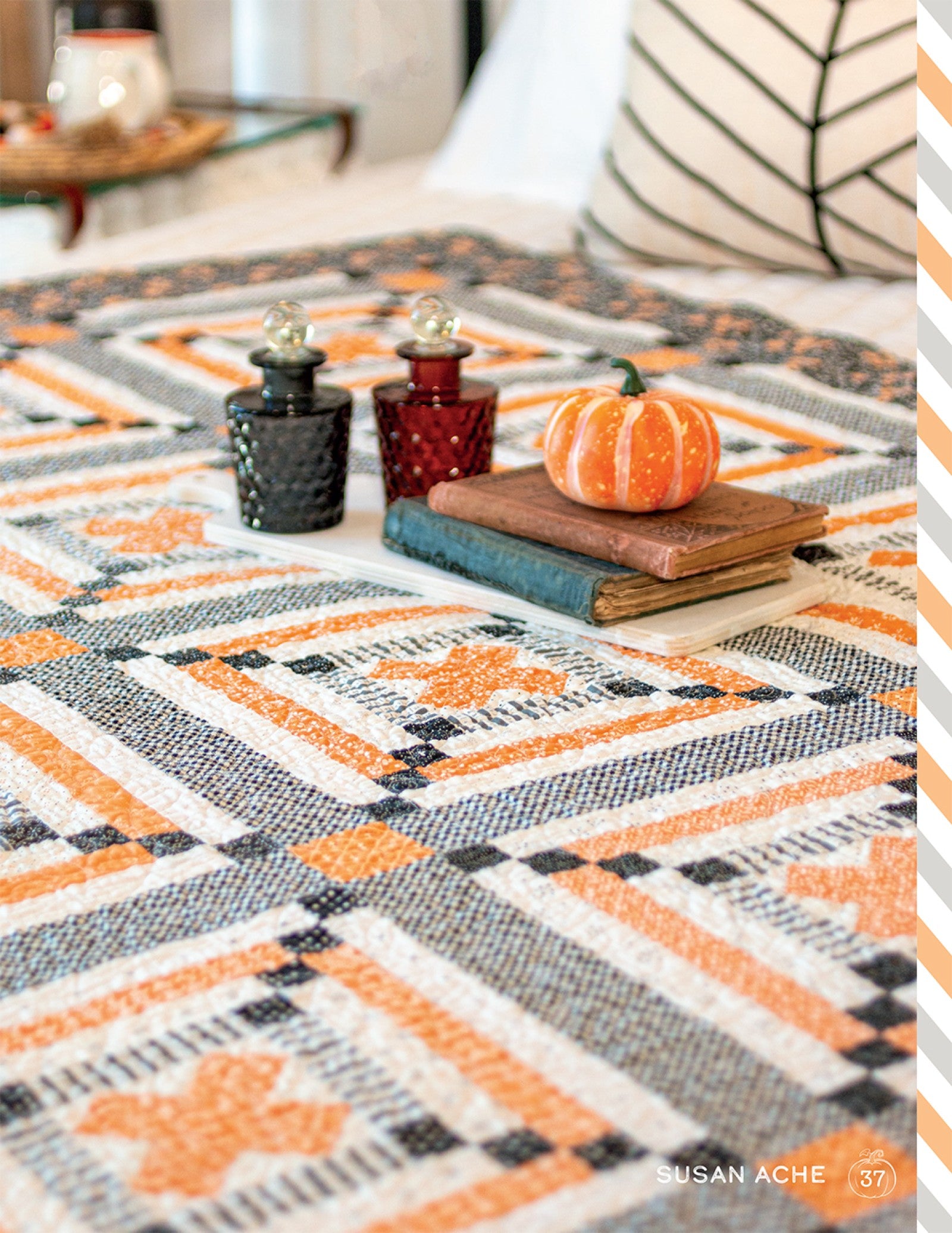 An orange, black, and cream Halloween quilt from Halloween Memories on a table with candlesticks and books.
