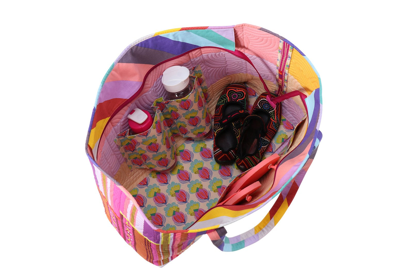 Top-down view inside a Two Big Tote packed for the beach, with a water bottle, sandals, and sunglasses held in the interior slip and zippered pockets.