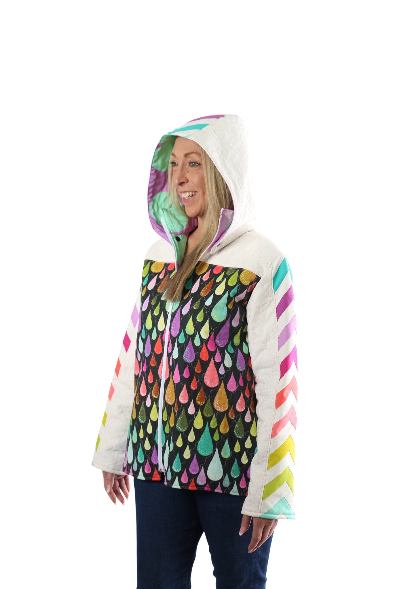 Front view of a person wearing a Bella Quilt Coat with the hood up over a colorful raindrop-print body, smiling.