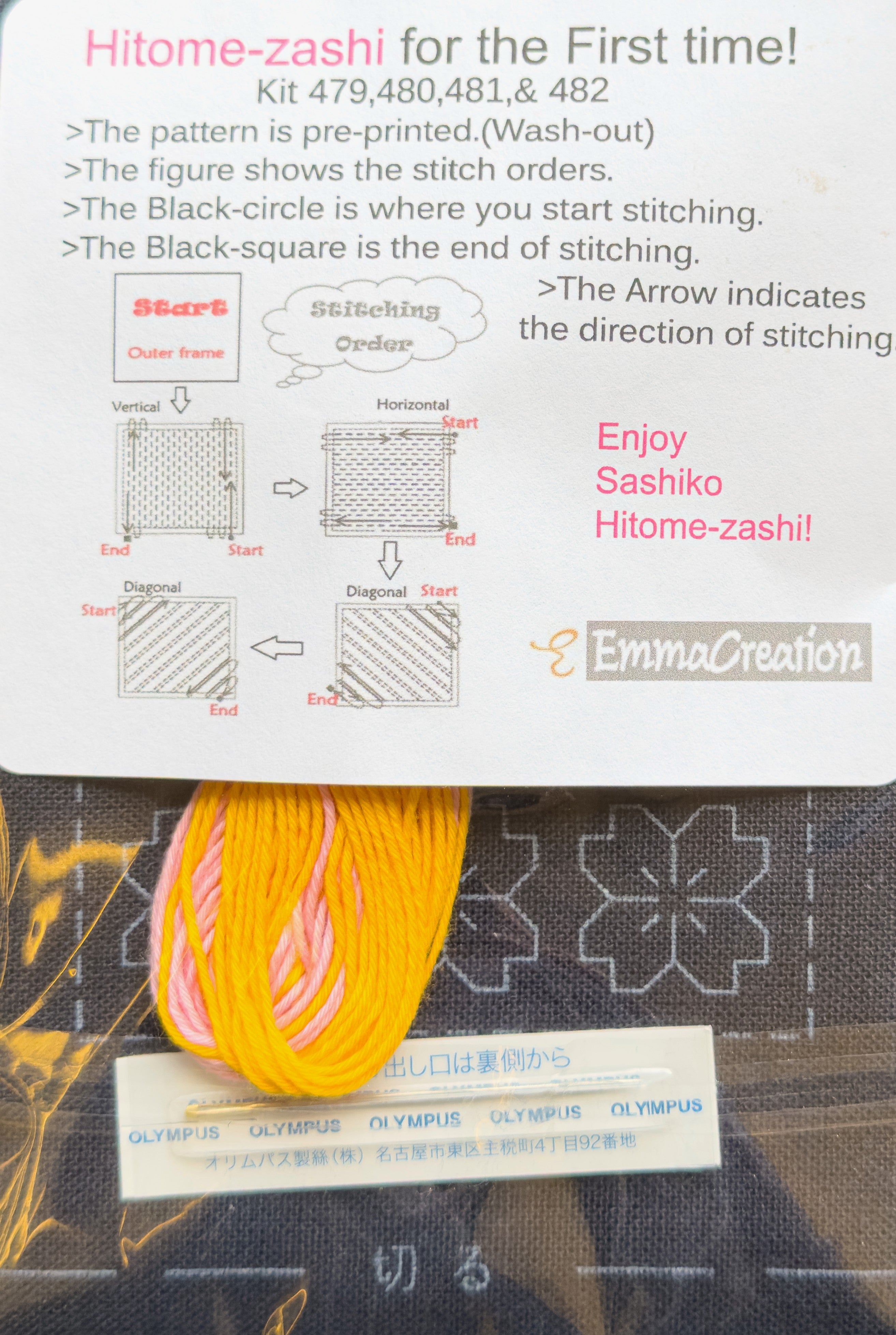 Contents of the Olympus hitomezashi sashiko coaster kit SK-0480 Tsubomi Navy from EmmaCreation: skeins of golden yellow and pale pink sashiko thread and an Olympus sashiko needle rest on the navy preprinted cloth, its sakura cherry blossom design showing in wash-out ink, beneath the EmmaCreation starter card diagramming the vertical, horizontal, and diagonal stitching order.