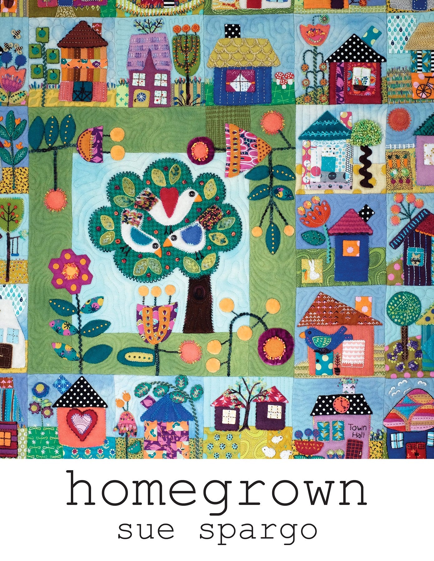 Front cover of Homegrown, a wool applique and embroidery quilt pattern book by Sue Spargo of Folk Art Quilts. The title sits over a folk art quilt of little houses, trees, flowers, and birds arranged around a central tree-of-life block, worked in bright wool with hand embroidery.